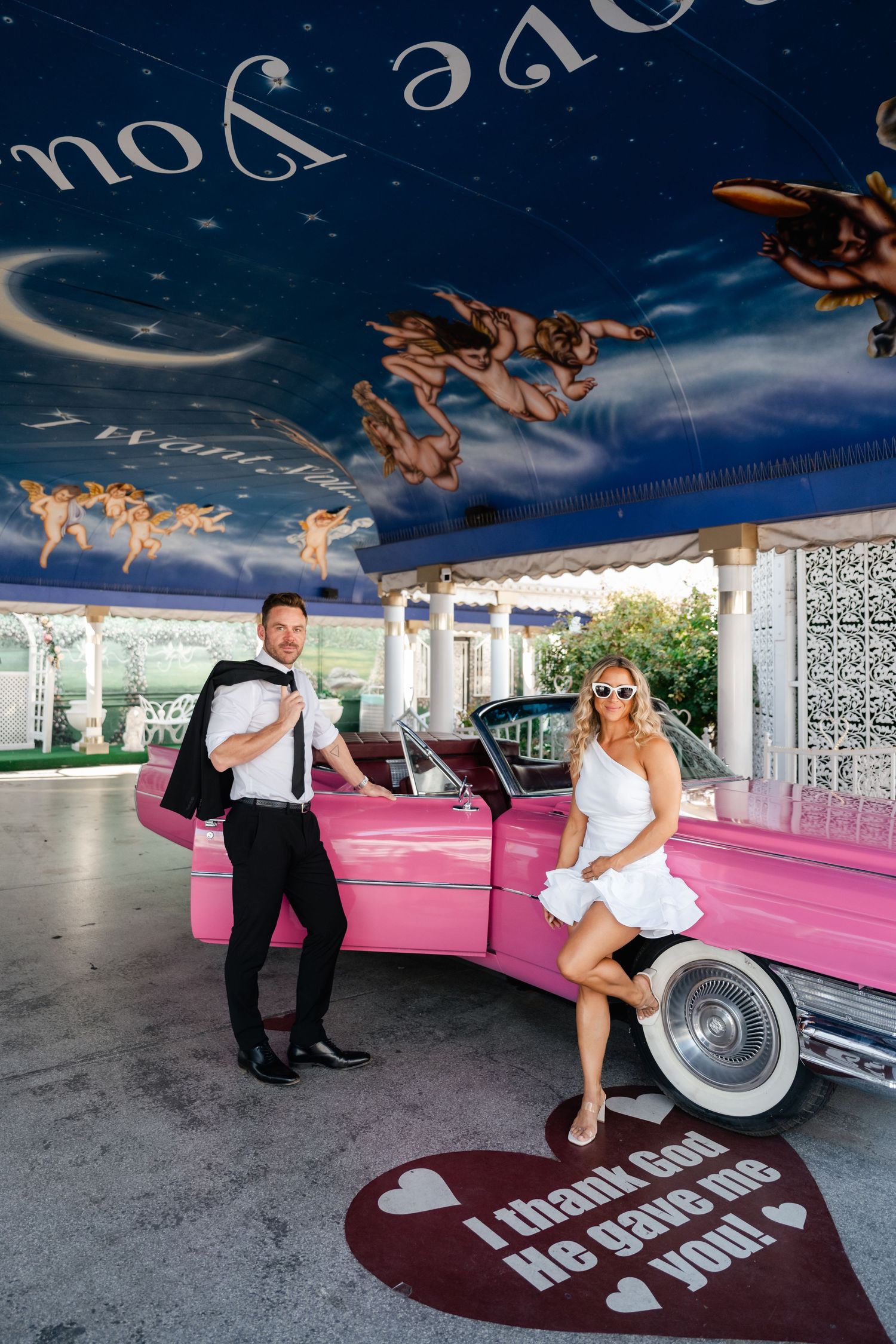 A couple poses playfully with a pink vintage car in a series of wedding photos under an outdoor pavilion. Las Vegas elopement photographer.