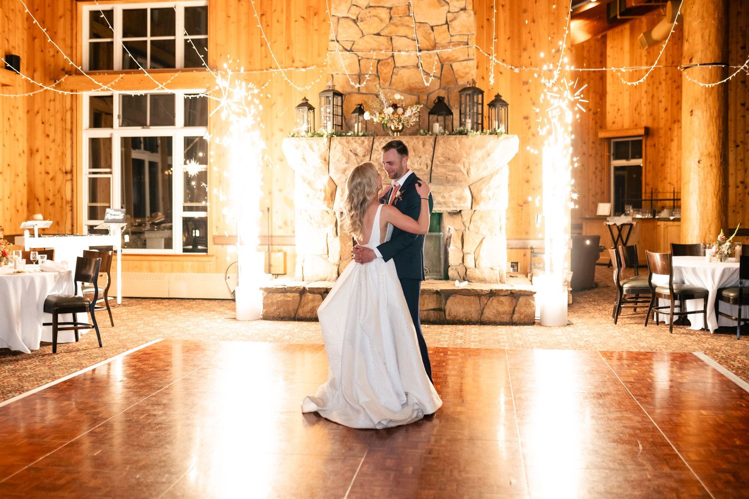 Wedding reception dancing in warmly lit rustic venue with wooden walls and large windows.