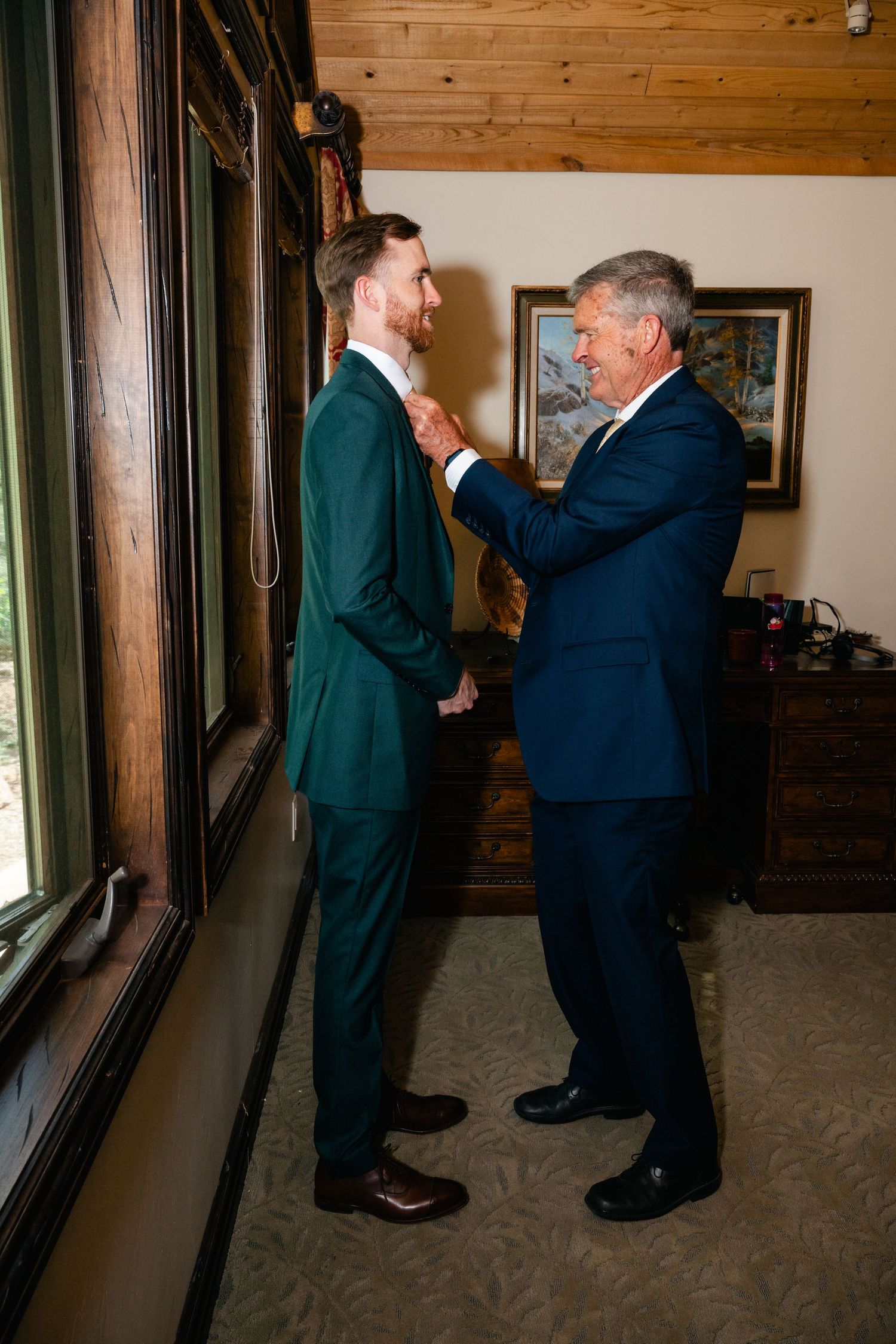 Two men in dark suits practicing dance steps together in a wood-paneled room.