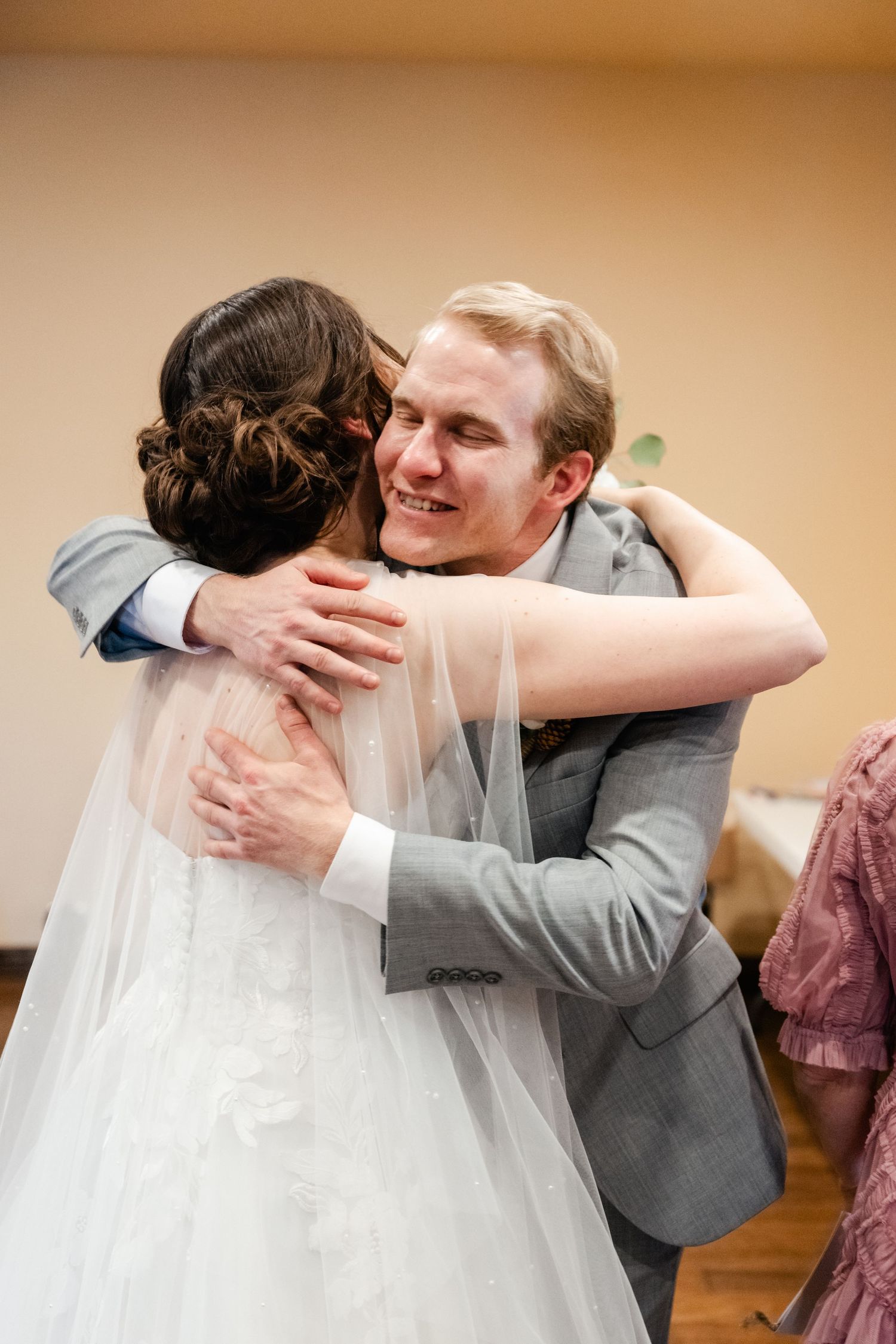 Tender embrace shared during wedding ceremony in indoor setting.