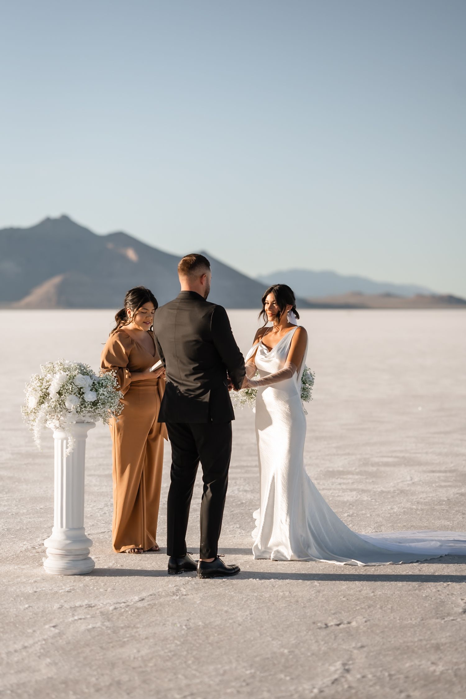 Wedding party stands together on salt flats with decorative white pillars and mountain backdrop.