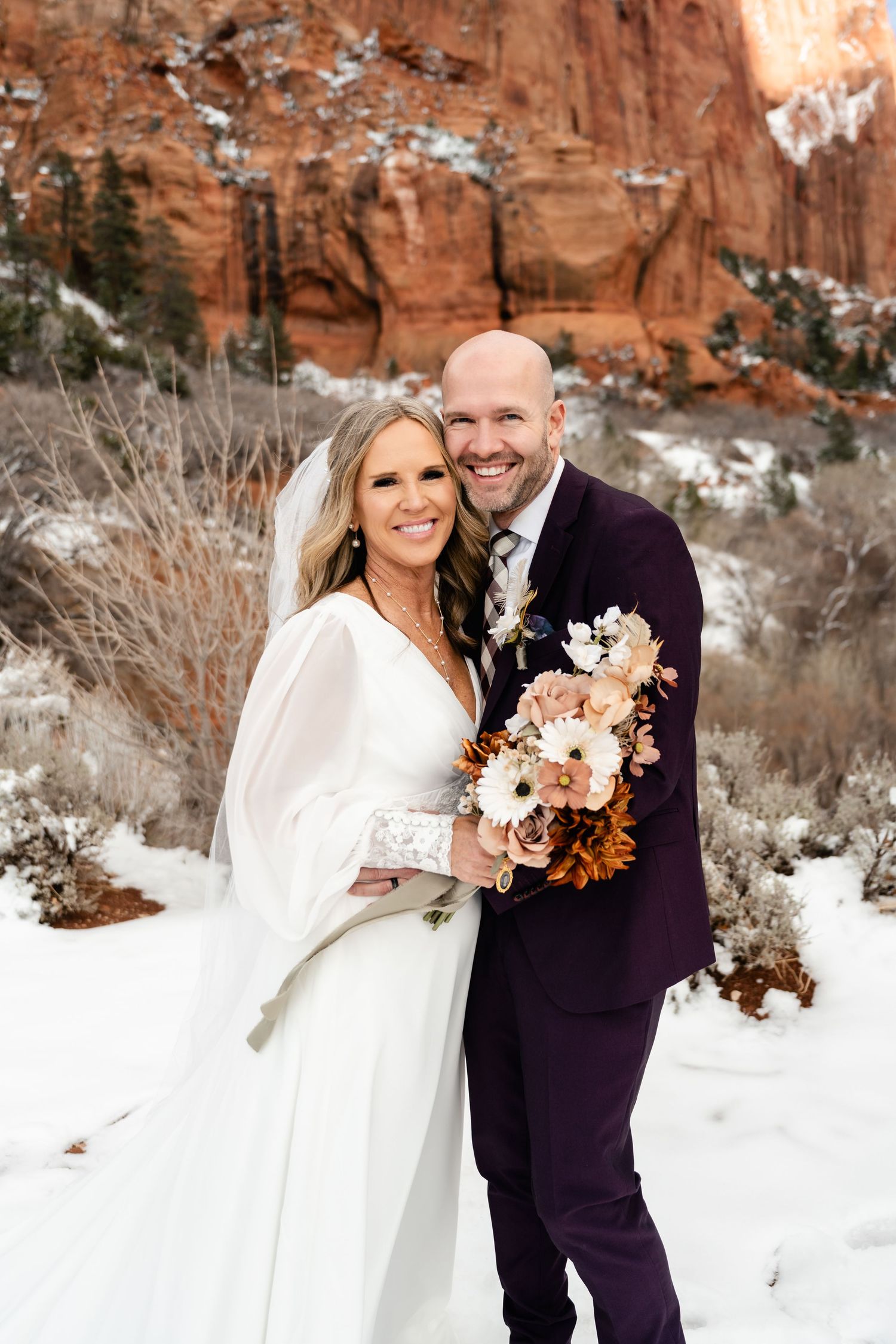 A winter wedding photo session against red rock cliffs with snow on the ground.
