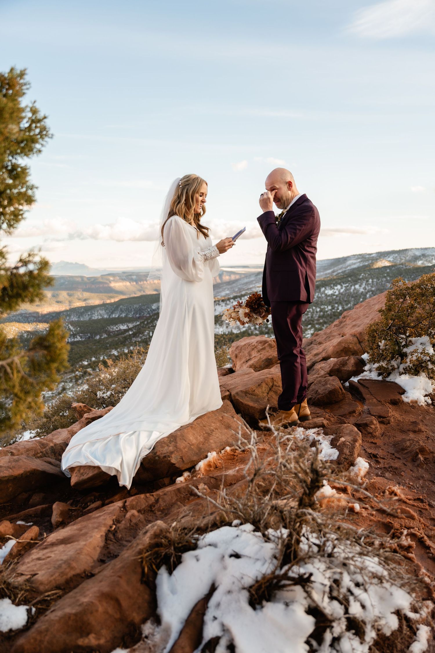 Couple shares emotional moment on snowy red rocks with mountain vistas in the background.