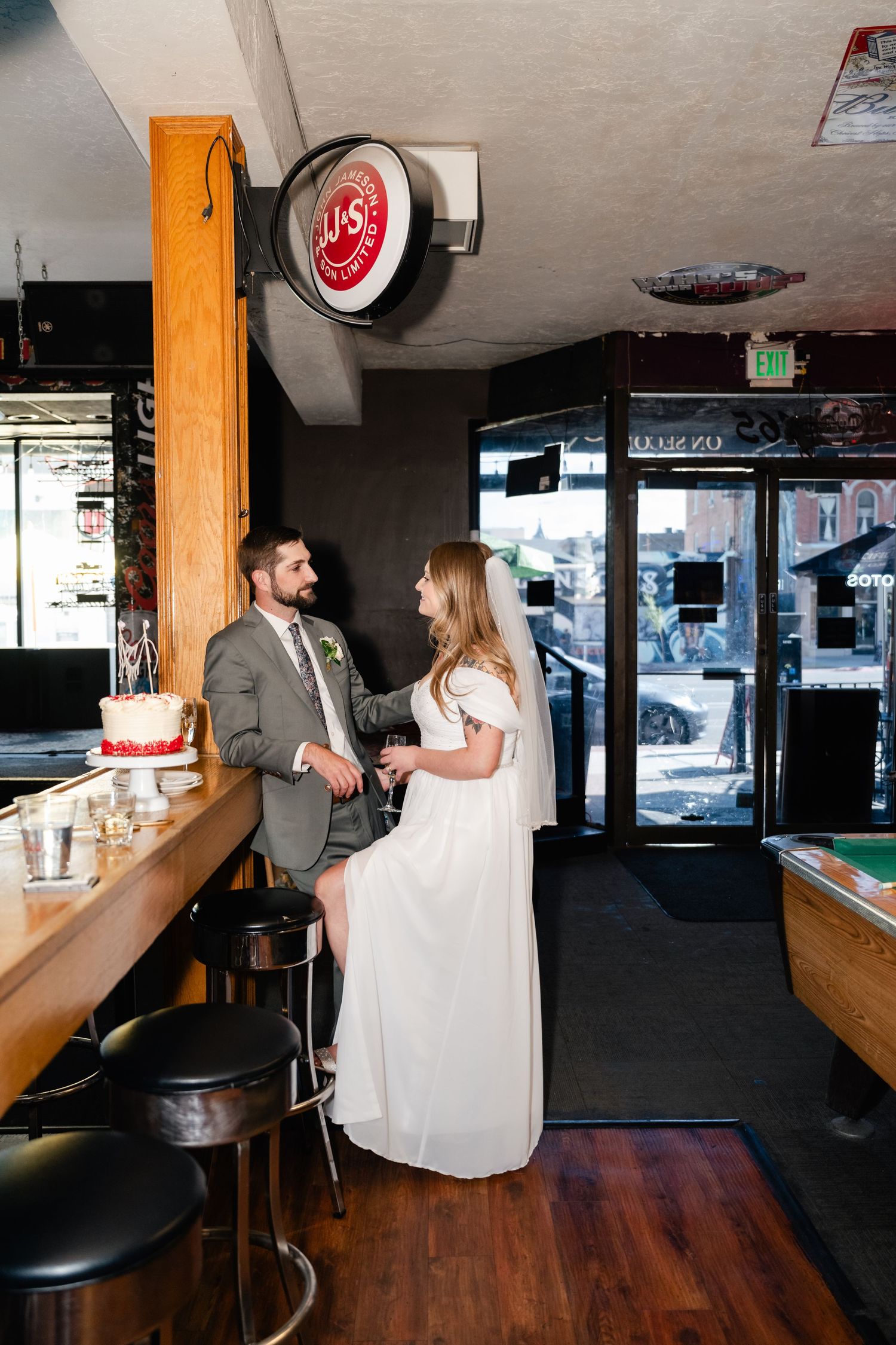 A couple in formal attire having drinks at a bar counter with neon signs and wood decor.