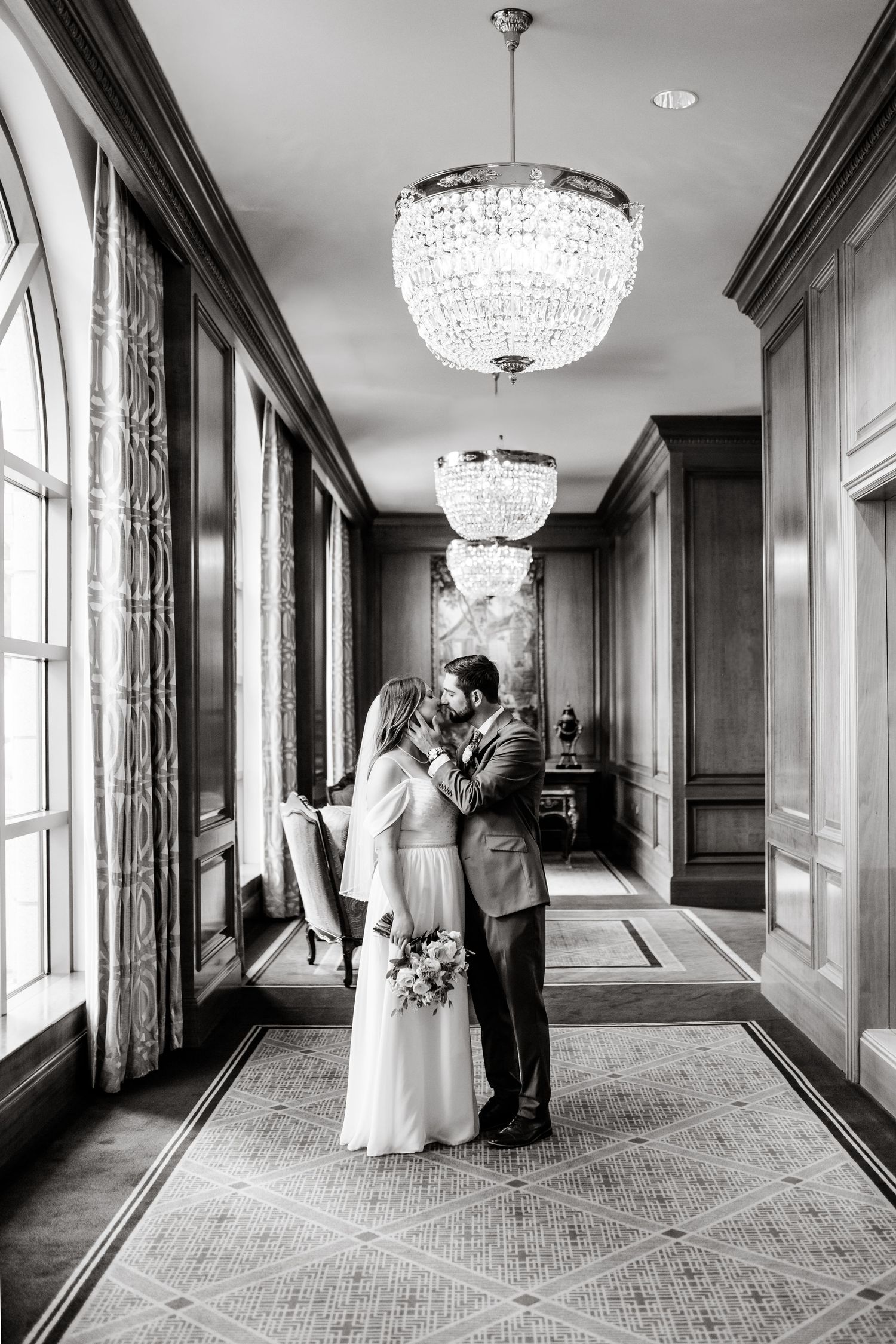 Romantic black and white wedding photos in elegant hallway with crystal chandeliers and large windows. Grand America Hotel Wedding.
