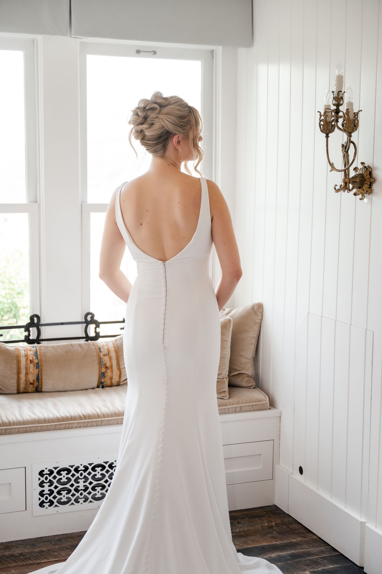 Back view of an elegant white wedding dress with open back detail in a bright room.
