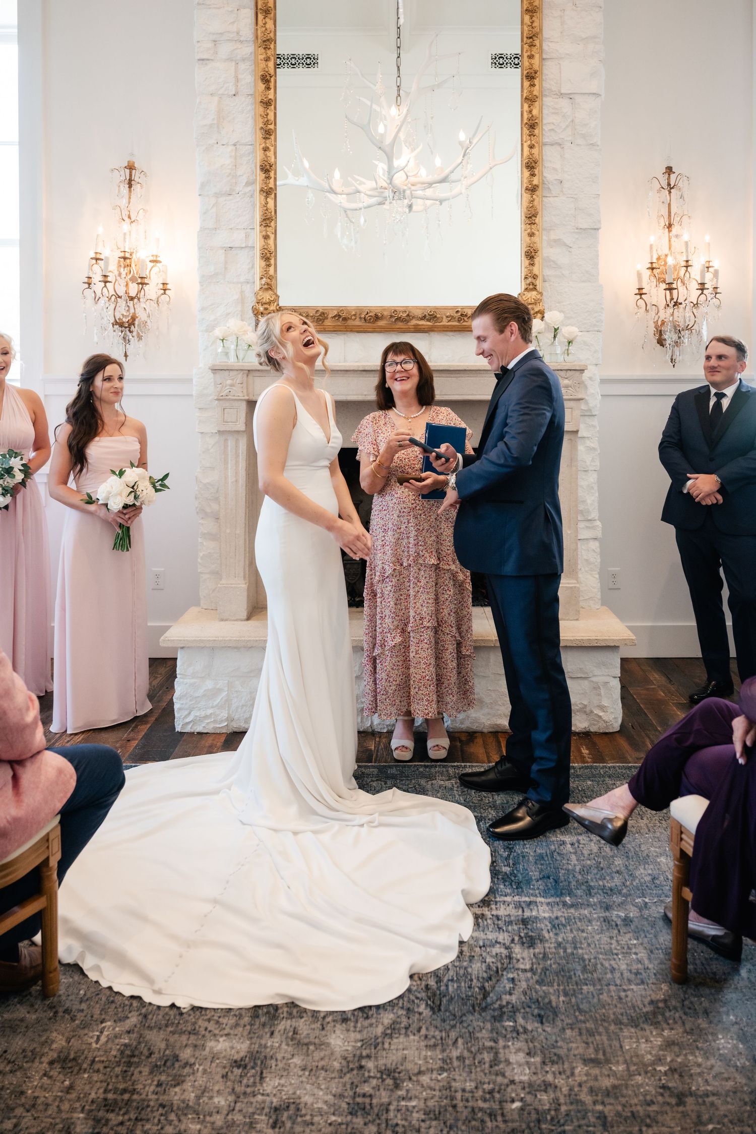 A wedding ceremony unfolds beneath a white antler chandelier and gold-framed mirror.