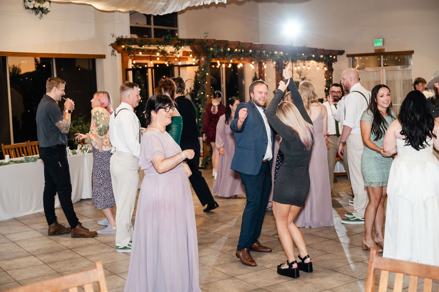 Wedding guests dancing and celebrating on a tiled dance floor at an indoor reception with decorative lighting.