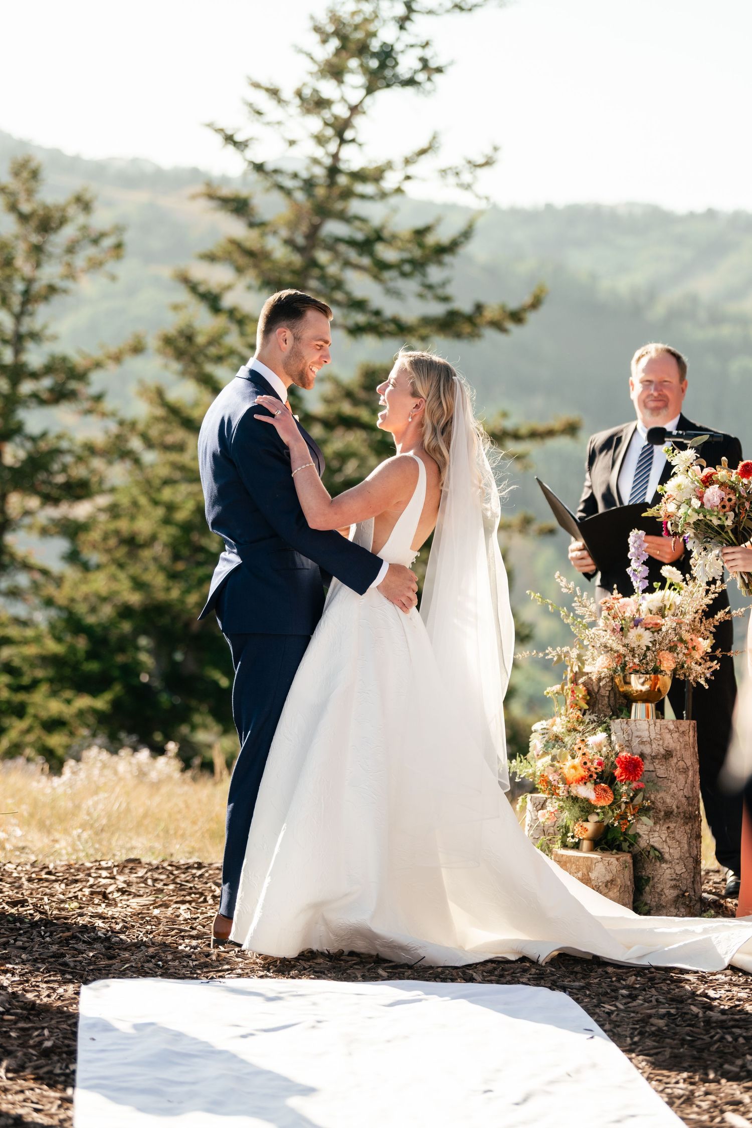 A couple shares a romantic moment during their mountaintop wedding ceremony with fall-colored floral arrangements. Park City Wedding Photo