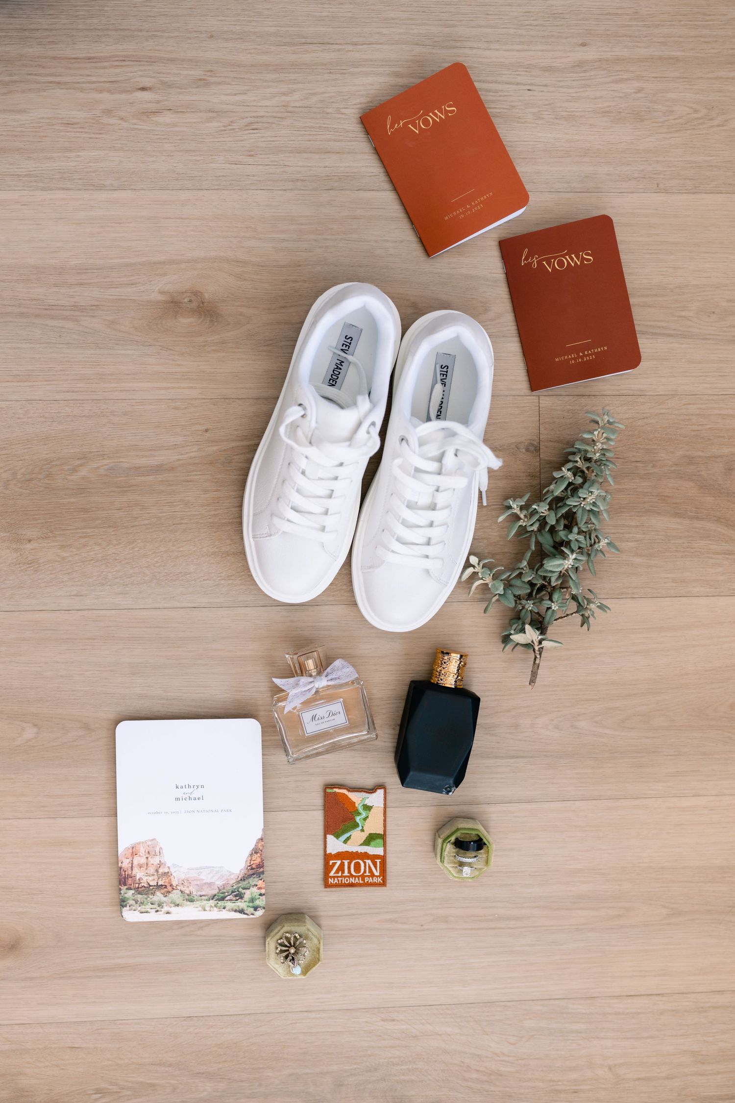 Wedding details flatlay with white sneakers, perfume, vow books and greenery on wooden background.