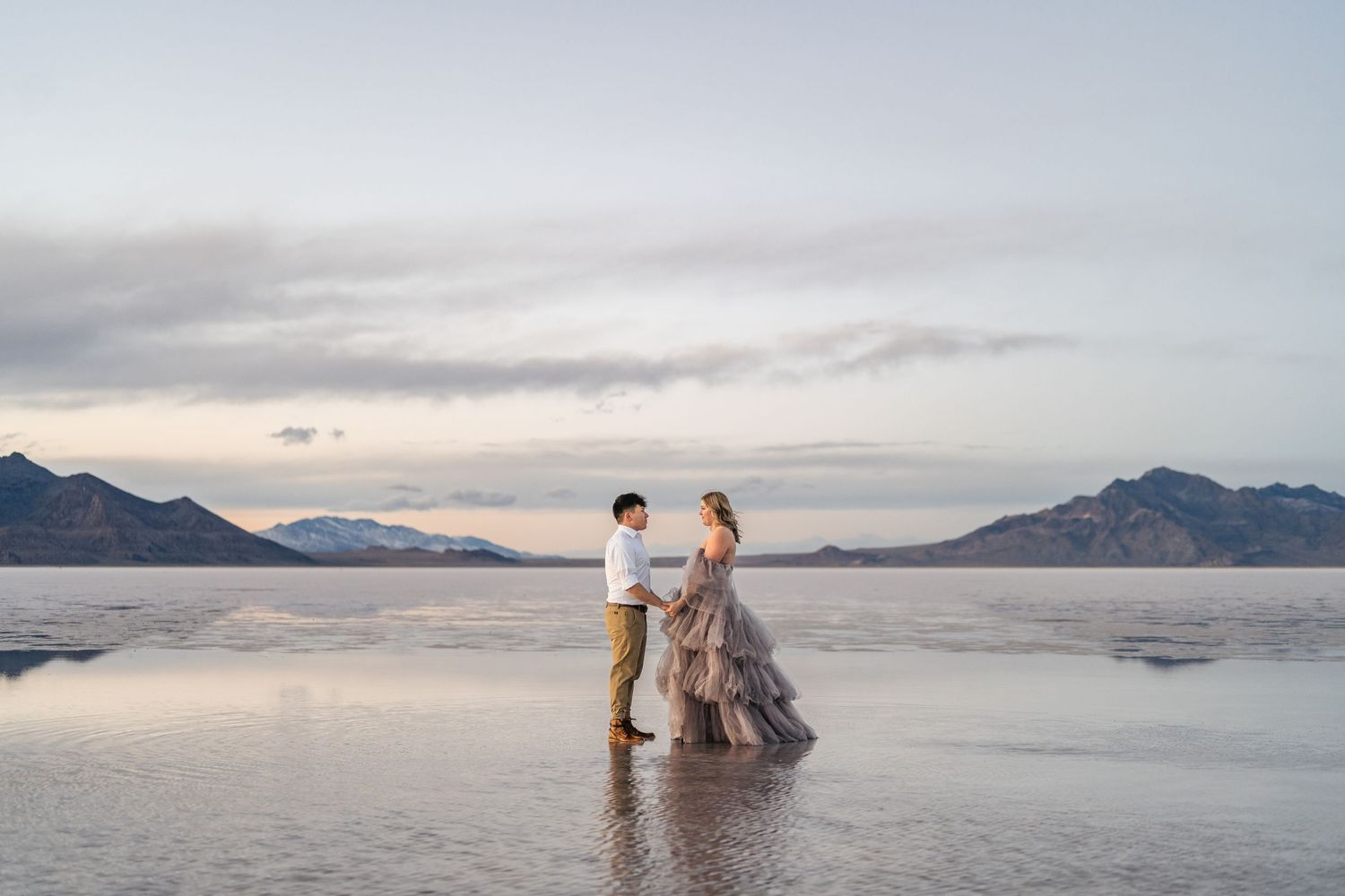 A couple holds hands as blue hour enhances the romance of a couple's photo session at the flooded Salt Flats.