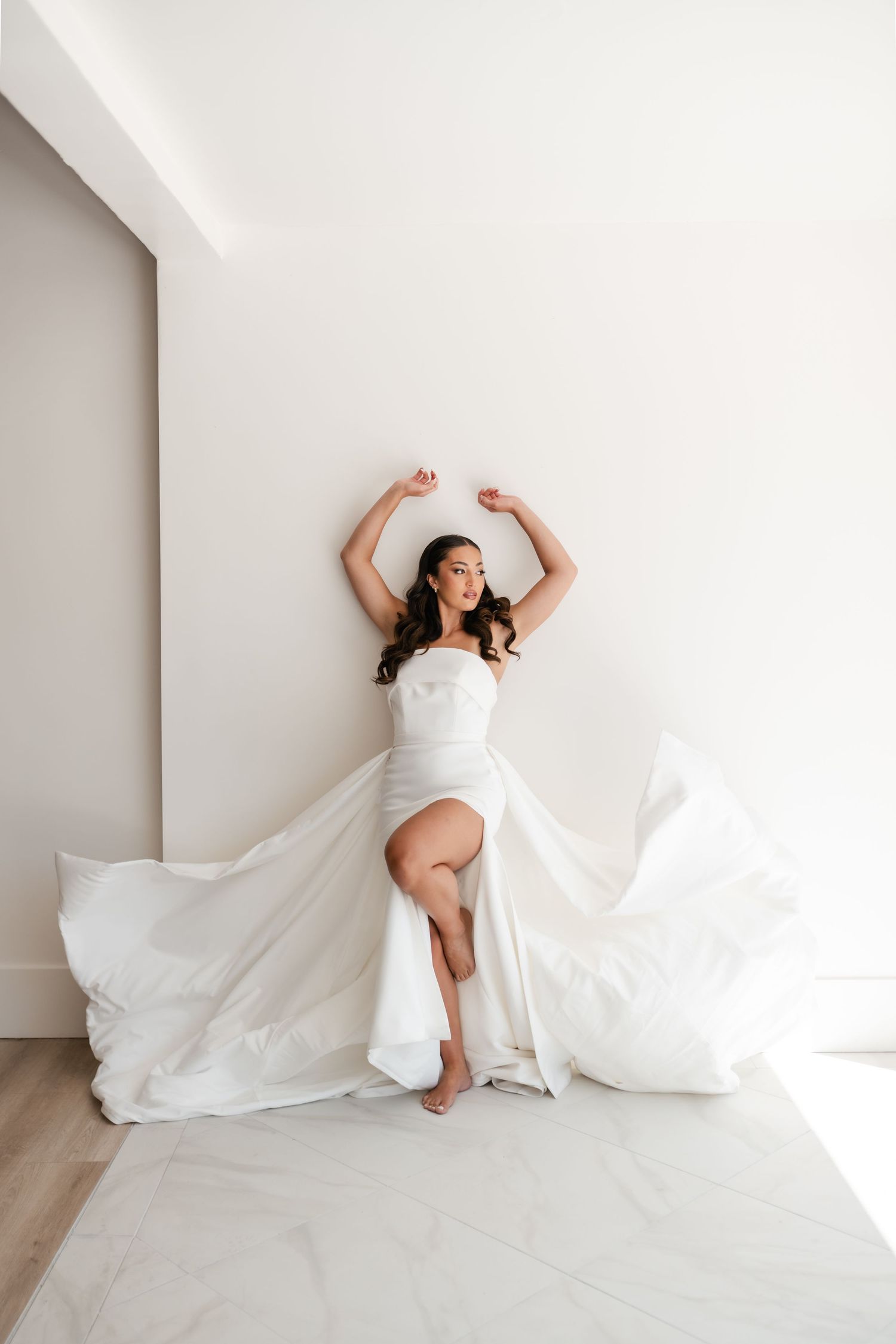 A bride in a flowing white dress strikes a graceful pose against a minimalist entry of Moments on Main. Utah Wedding Photographer.