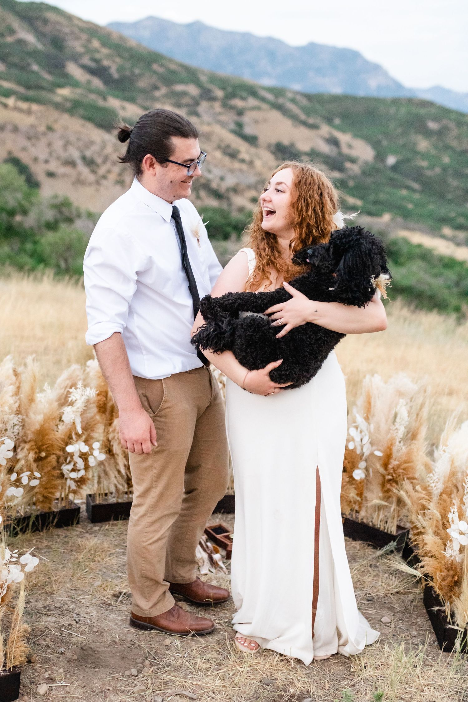 A couple stands together in a field of tall grass with mountains in the background. Utah mountain elopement photographer.