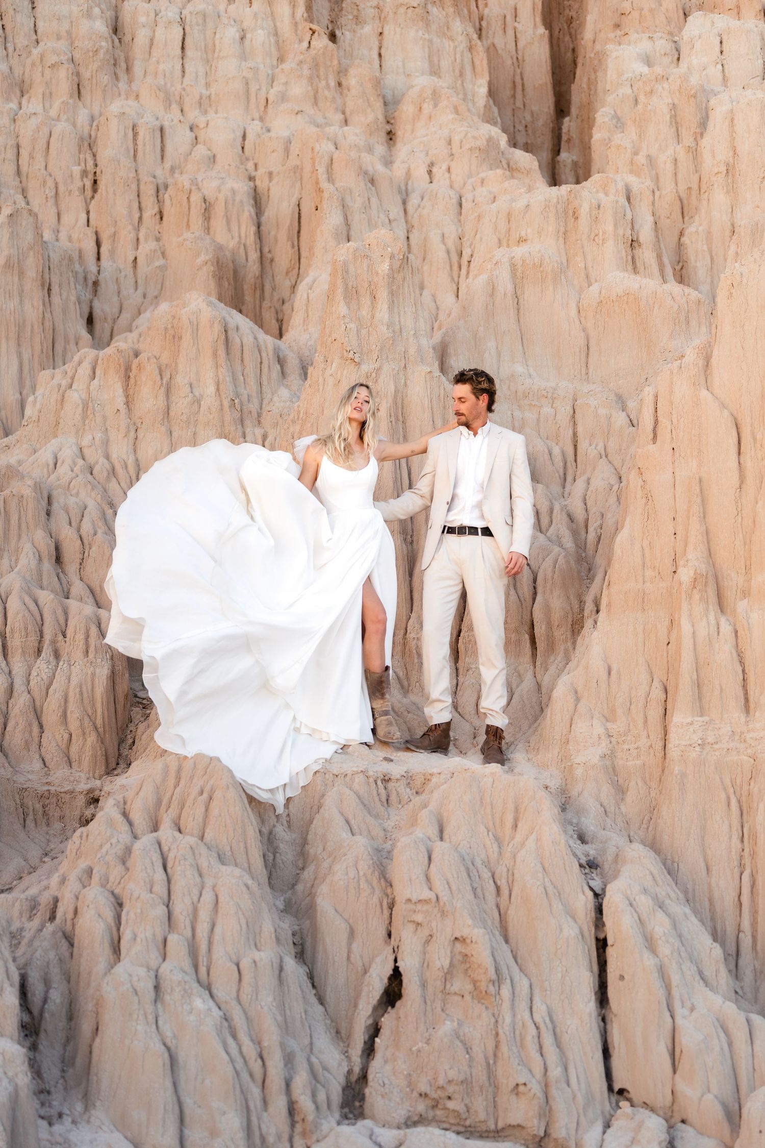 A romantic wedding photoshoot against a textured beige rock formation with flowing white dress and elegant poses. Cathedral Gorge Photograph