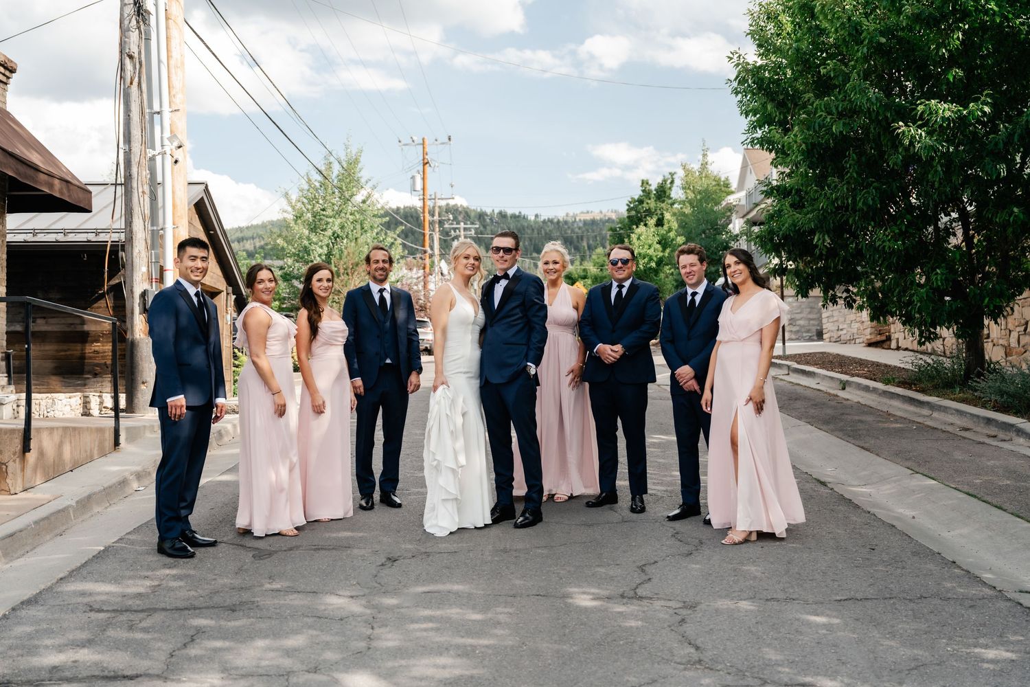 Wedding party poses together on a city street with brick buildings and utility poles in the background.