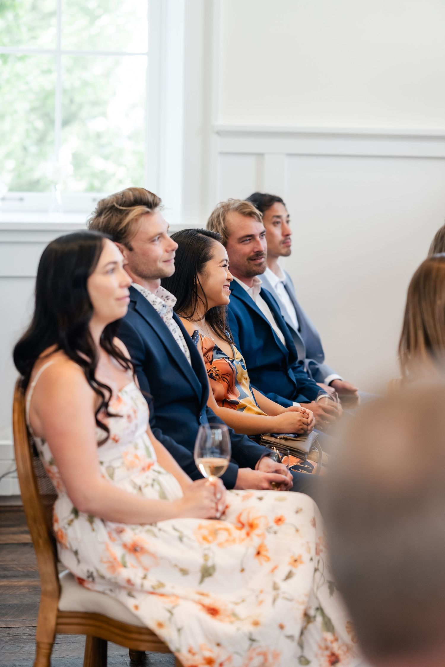 Guests in formal attire react with laughter while seated in rows at an indoor event.