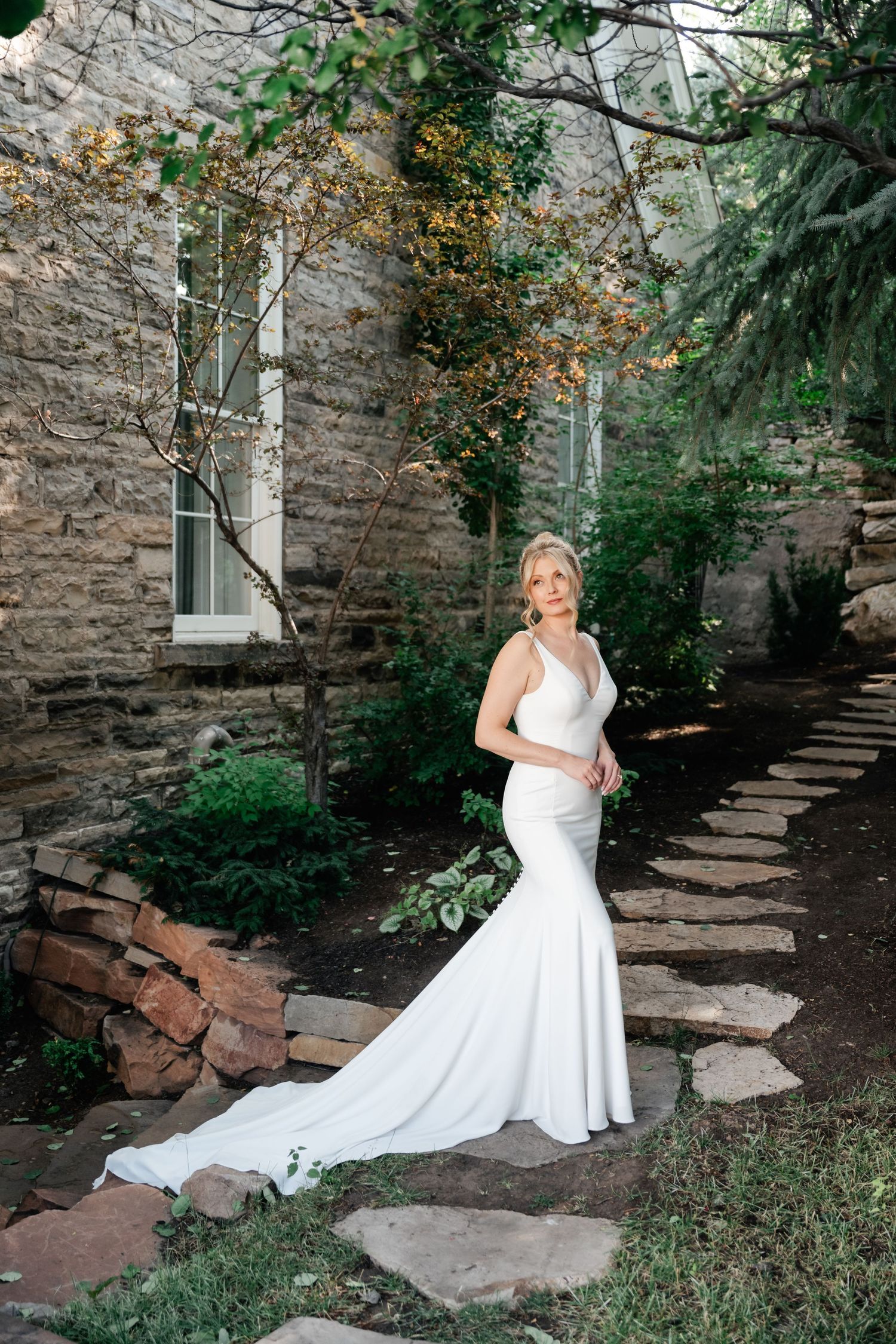 A flowing white wedding gown photographed against a rustic stone wall and garden pathway.
