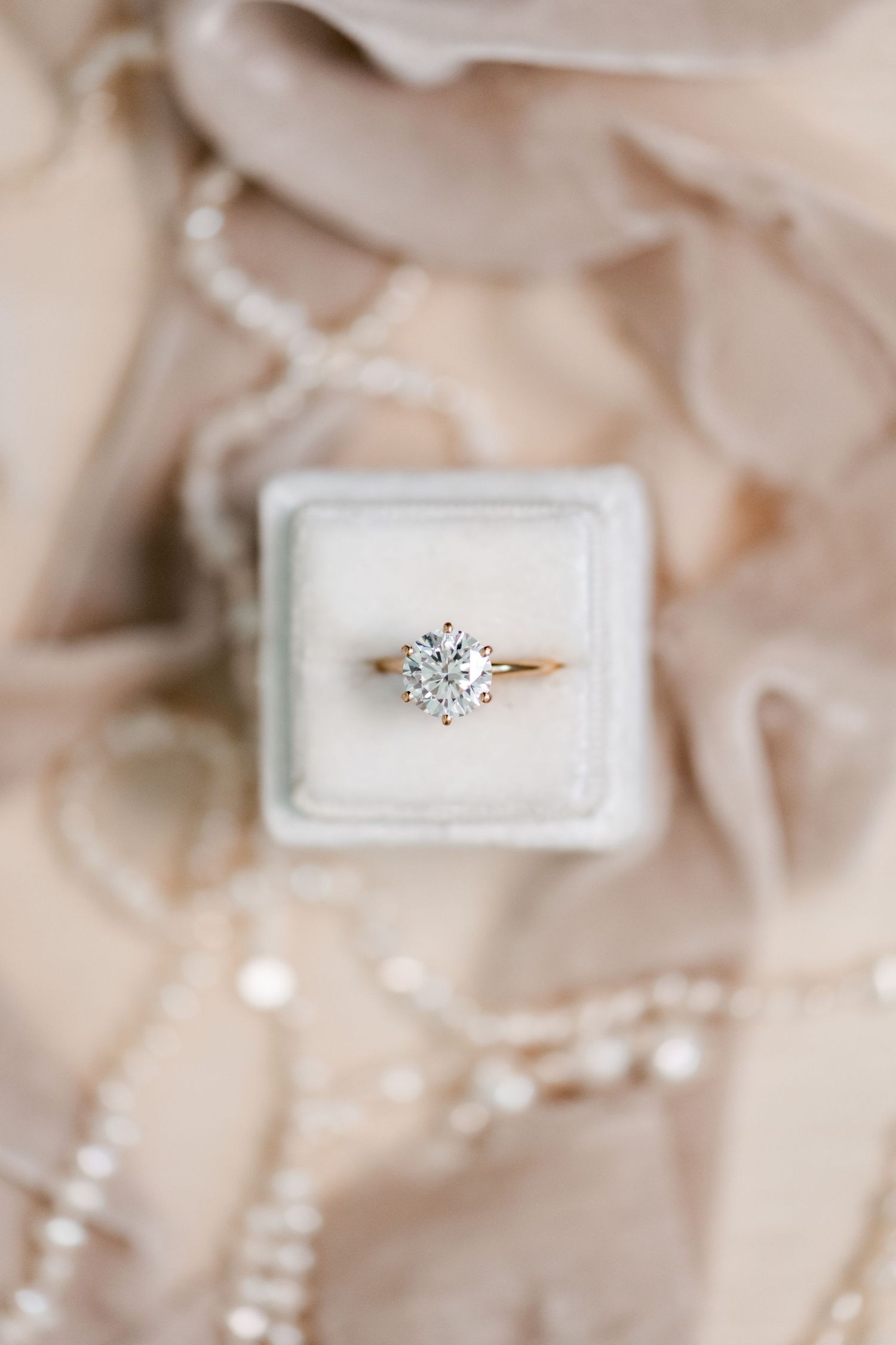 Elegant diamond engagement ring in a white box displayed on beige fabric.