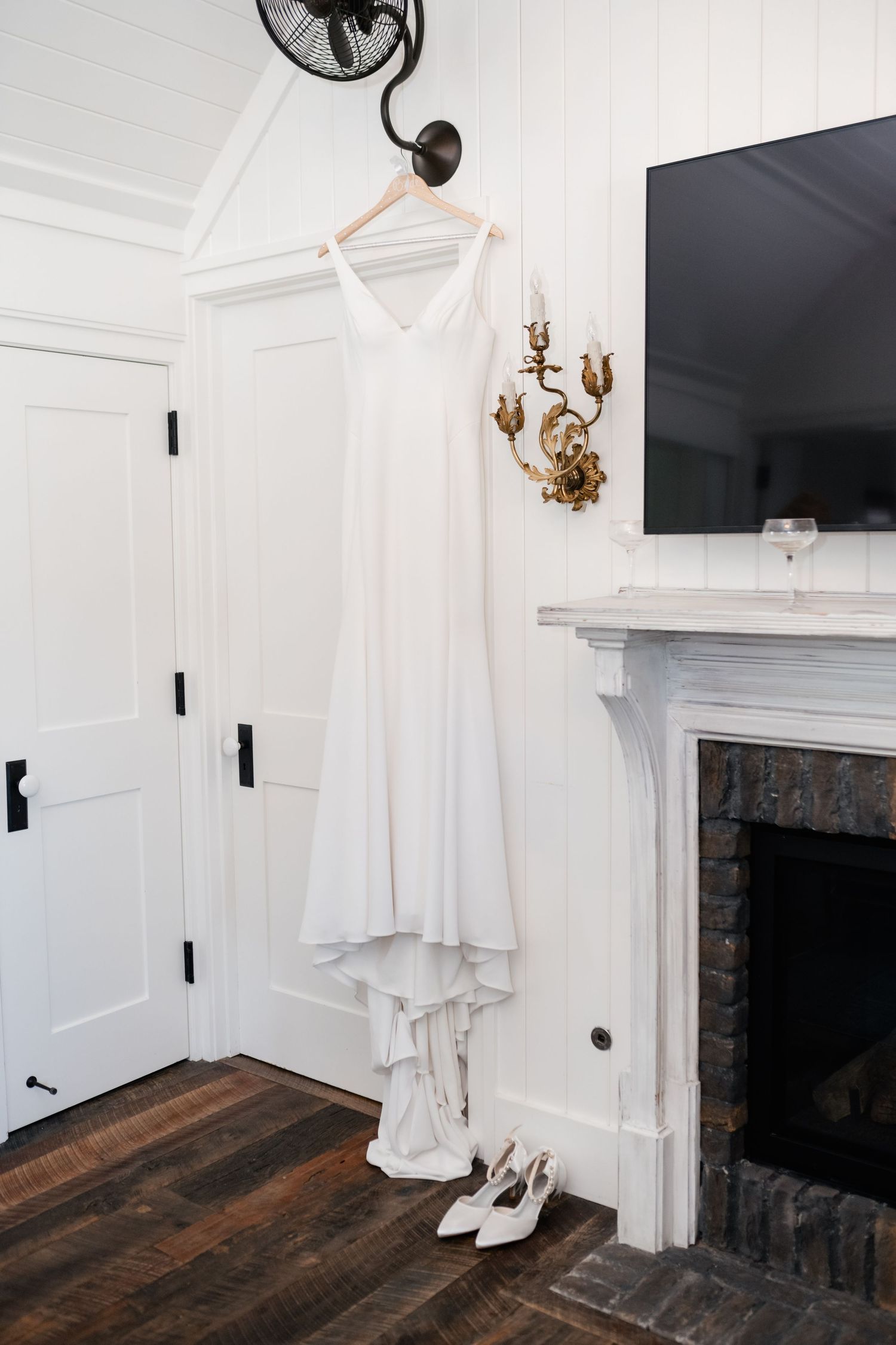 White wedding dress hanging in modern room with white walls and dark wood floors.