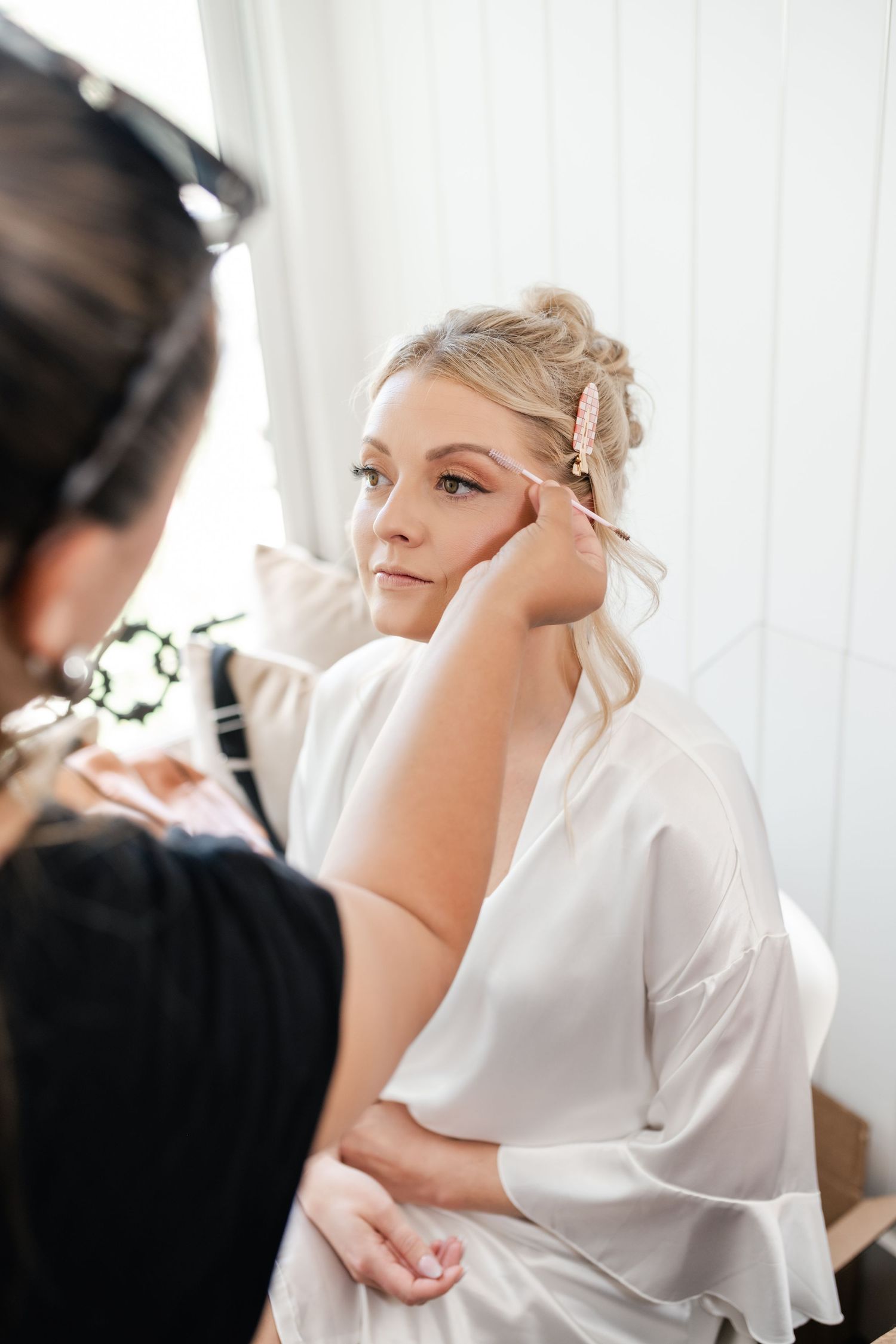 Wedding preparation scene with makeup application in bright white room.