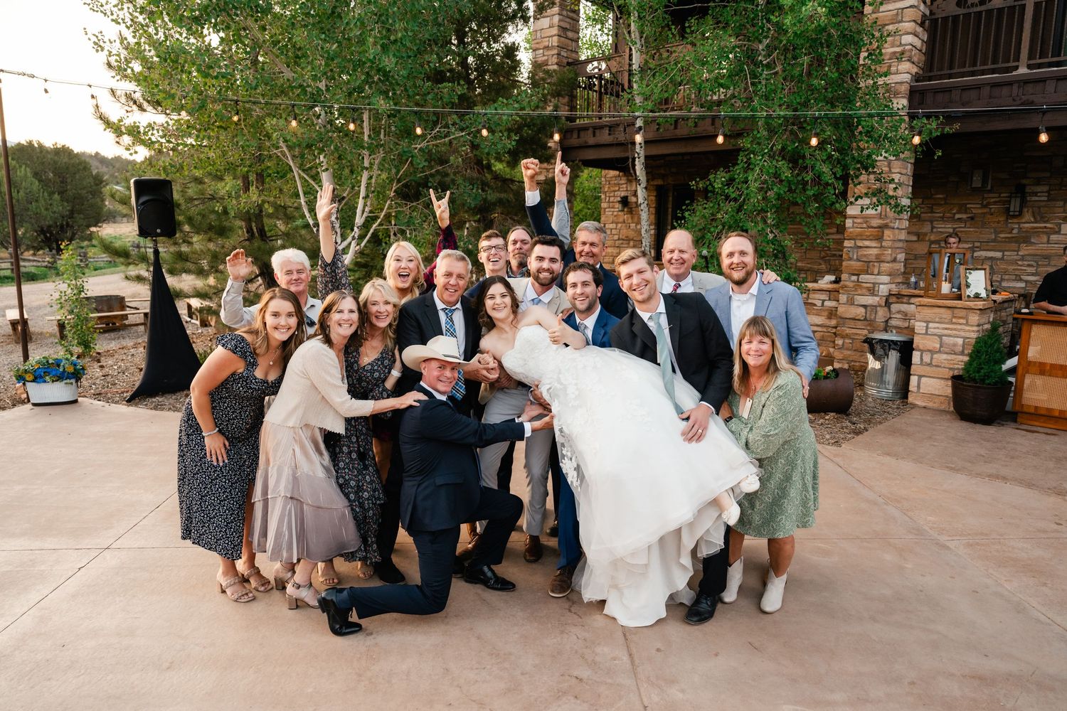 Wedding guests gather in small groups on a brick patio during an outdoor evening reception celebration.