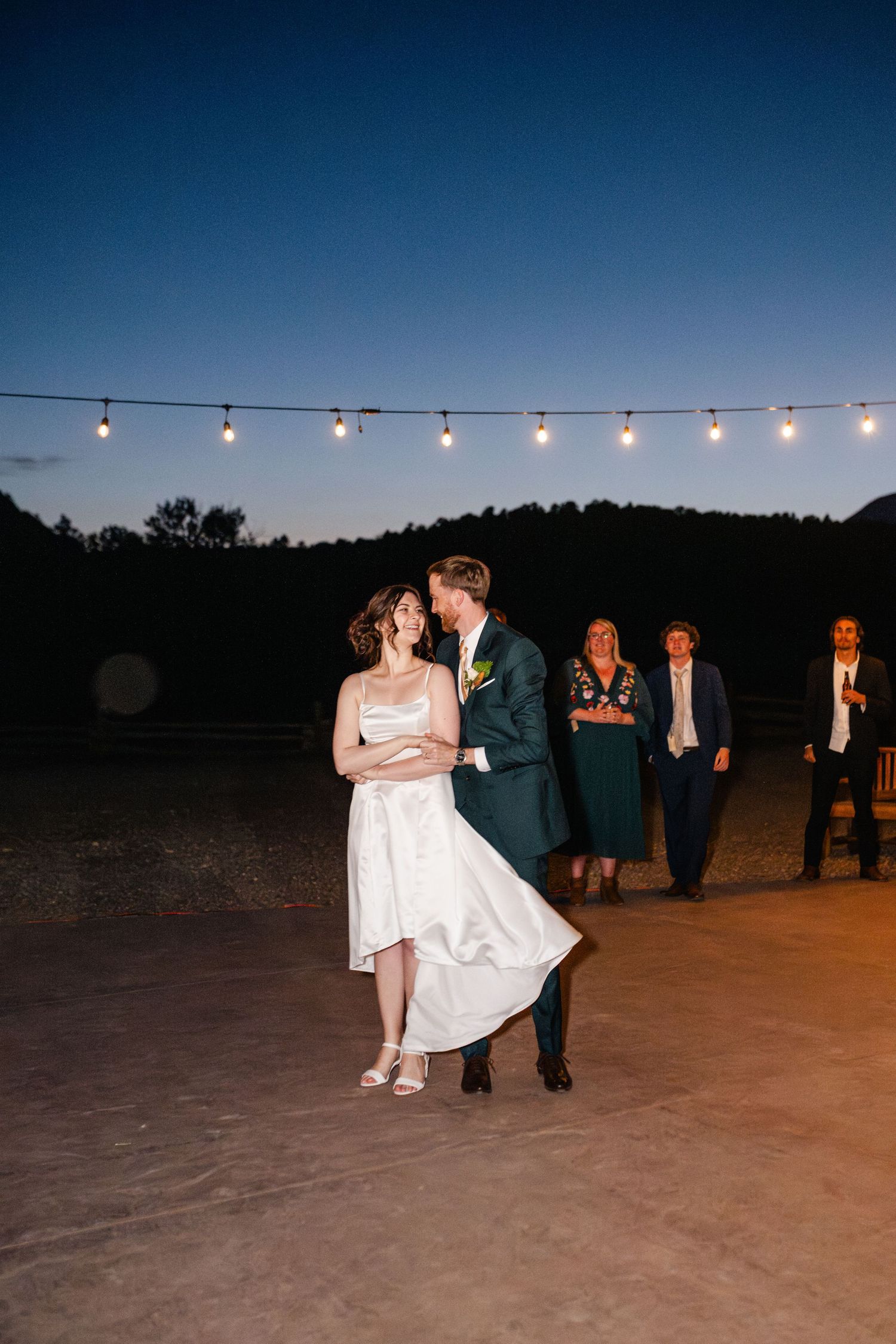 Couple shares intimate dance moment under string lights at dusk.