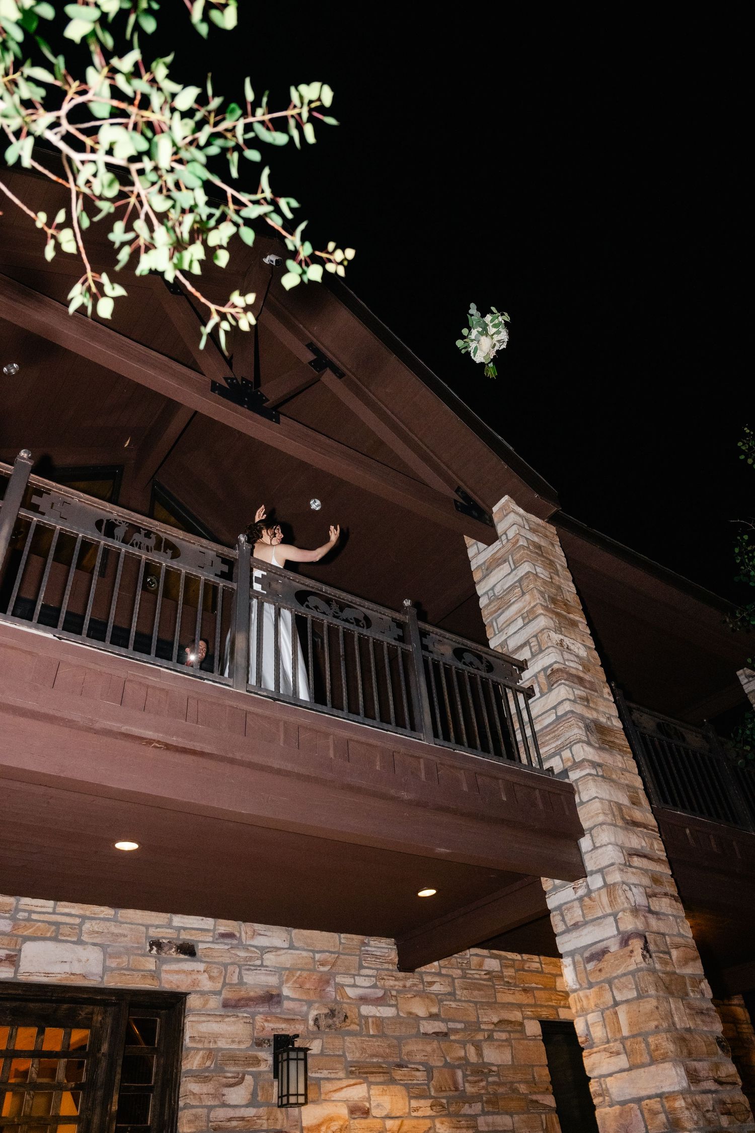 Stone pillars and balcony of a rustic venue illuminated at night with hanging greenery.