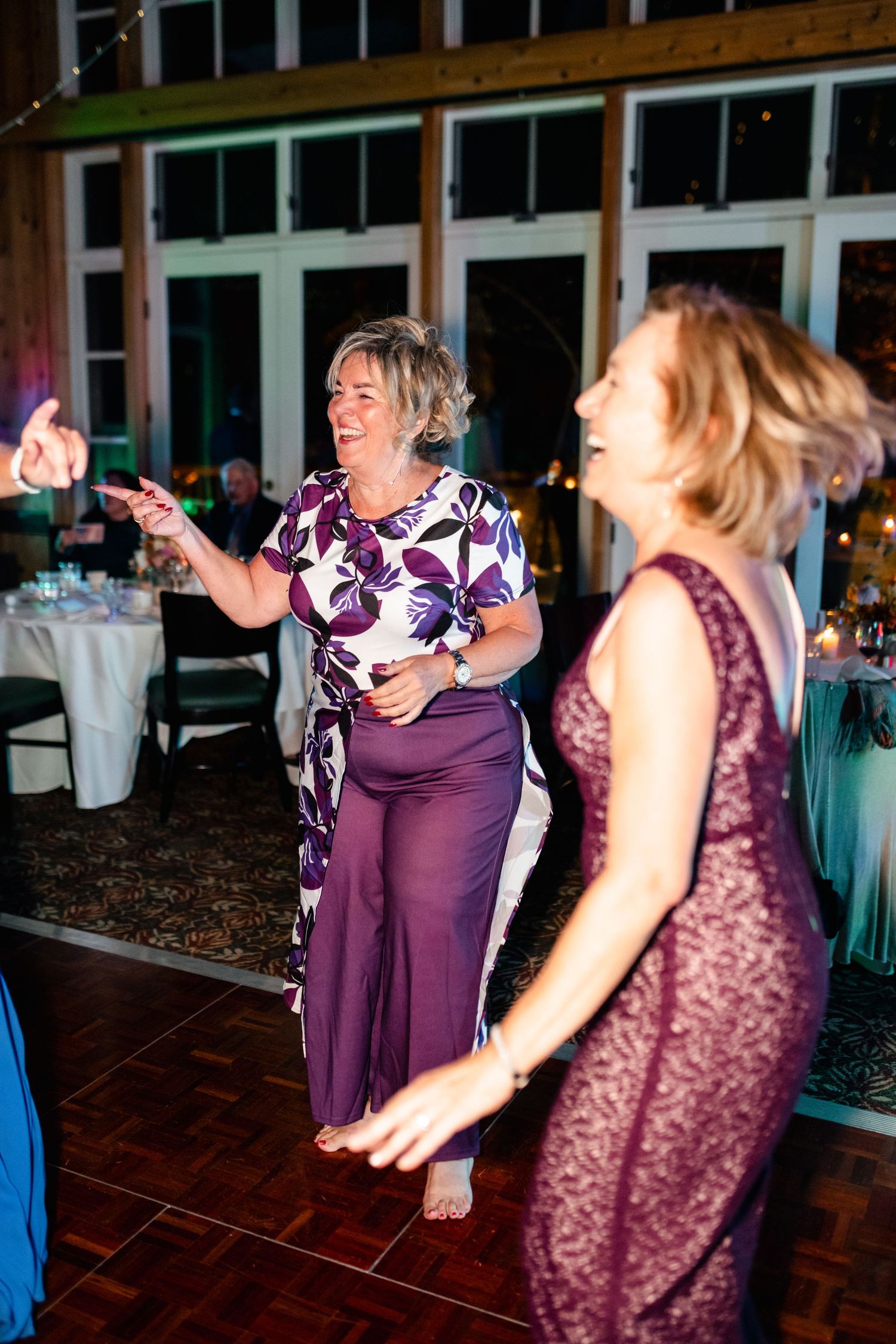 Wedding guests in purple dresses dancing enthusiastically at reception.