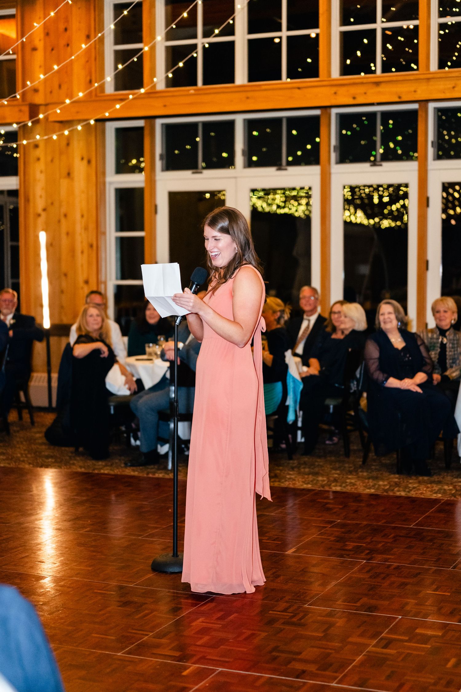 Wedding reception speech in rustic wooden venue with string lights and warm ambiance.