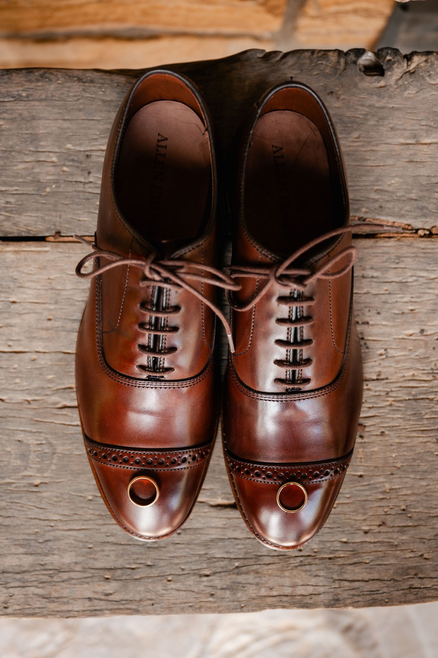 Classic brown leather oxford dress shoes photographed on weathered wooden surface.