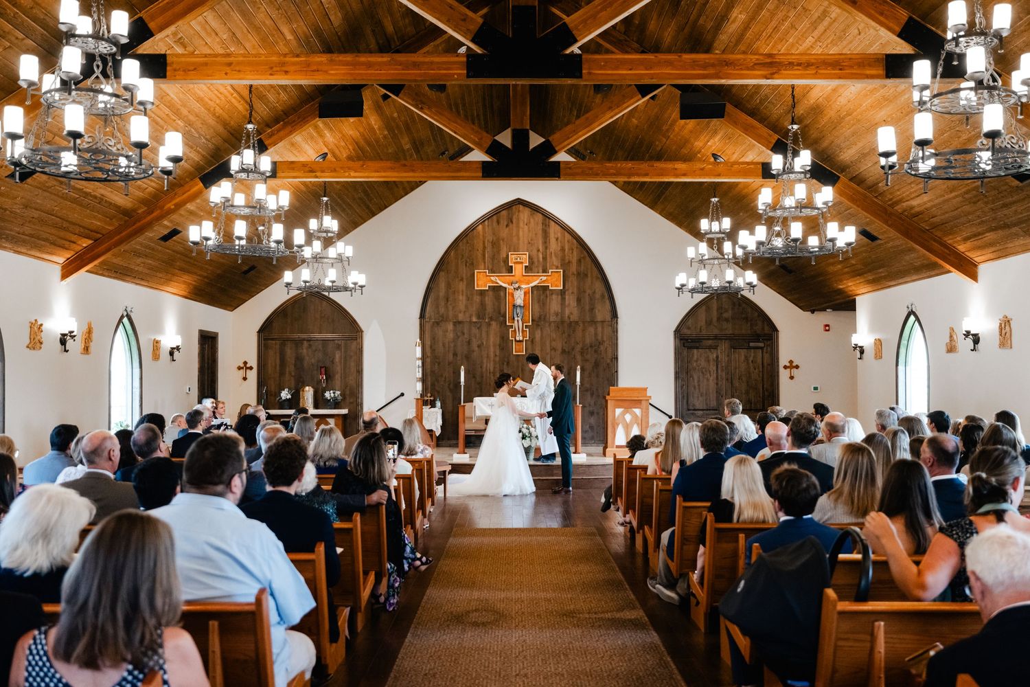 Traditional church wedding ceremony taking place in a chapel with wooden beams and elegant chandeliers.