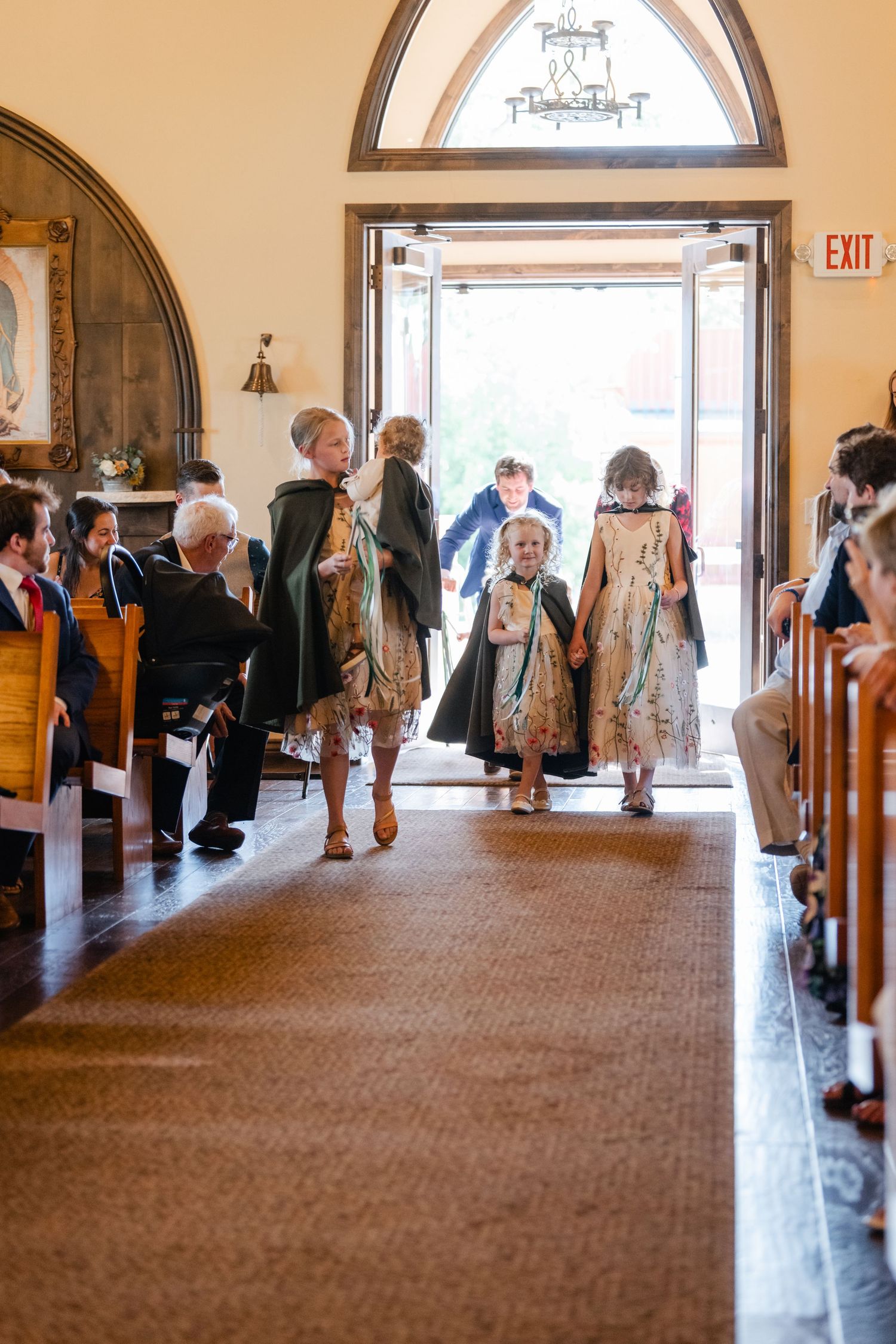 Wedding guests gather in a church hallway with arched doorways and warm lighting.