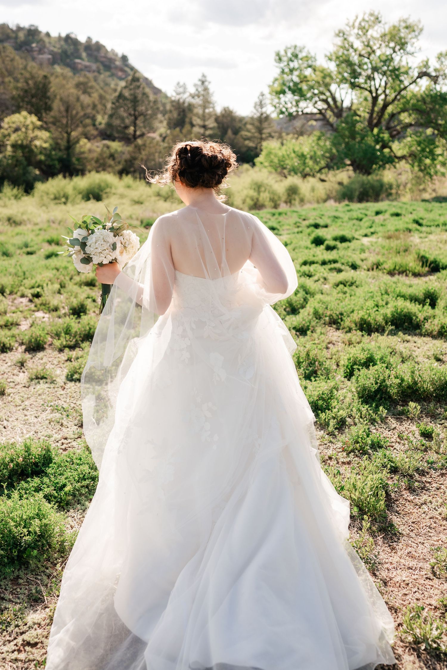 Flowing white wedding dress train trailing behind on green desert landscape.