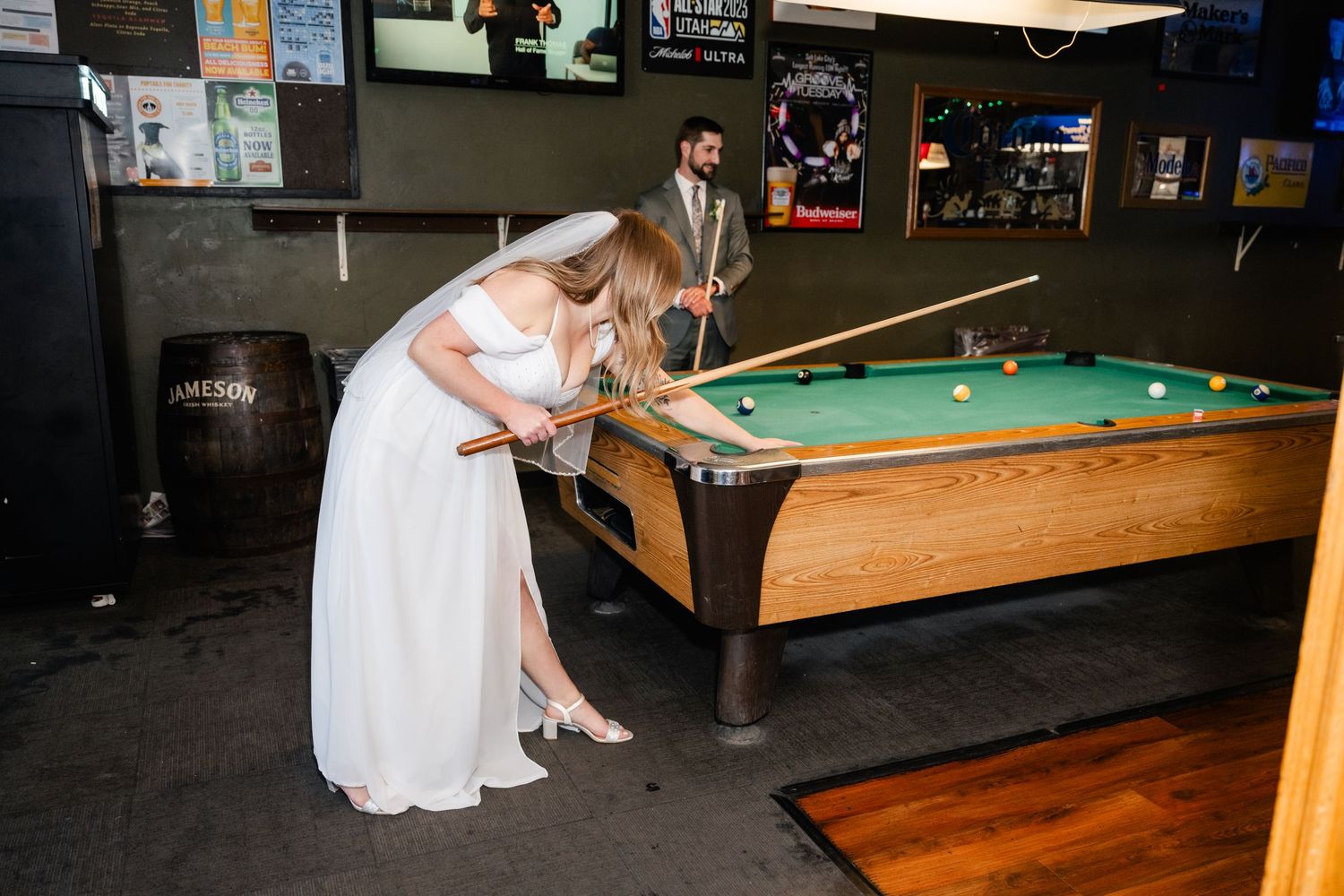 A romantic couple poses playfully by a pool table in a dimly lit bar setting.