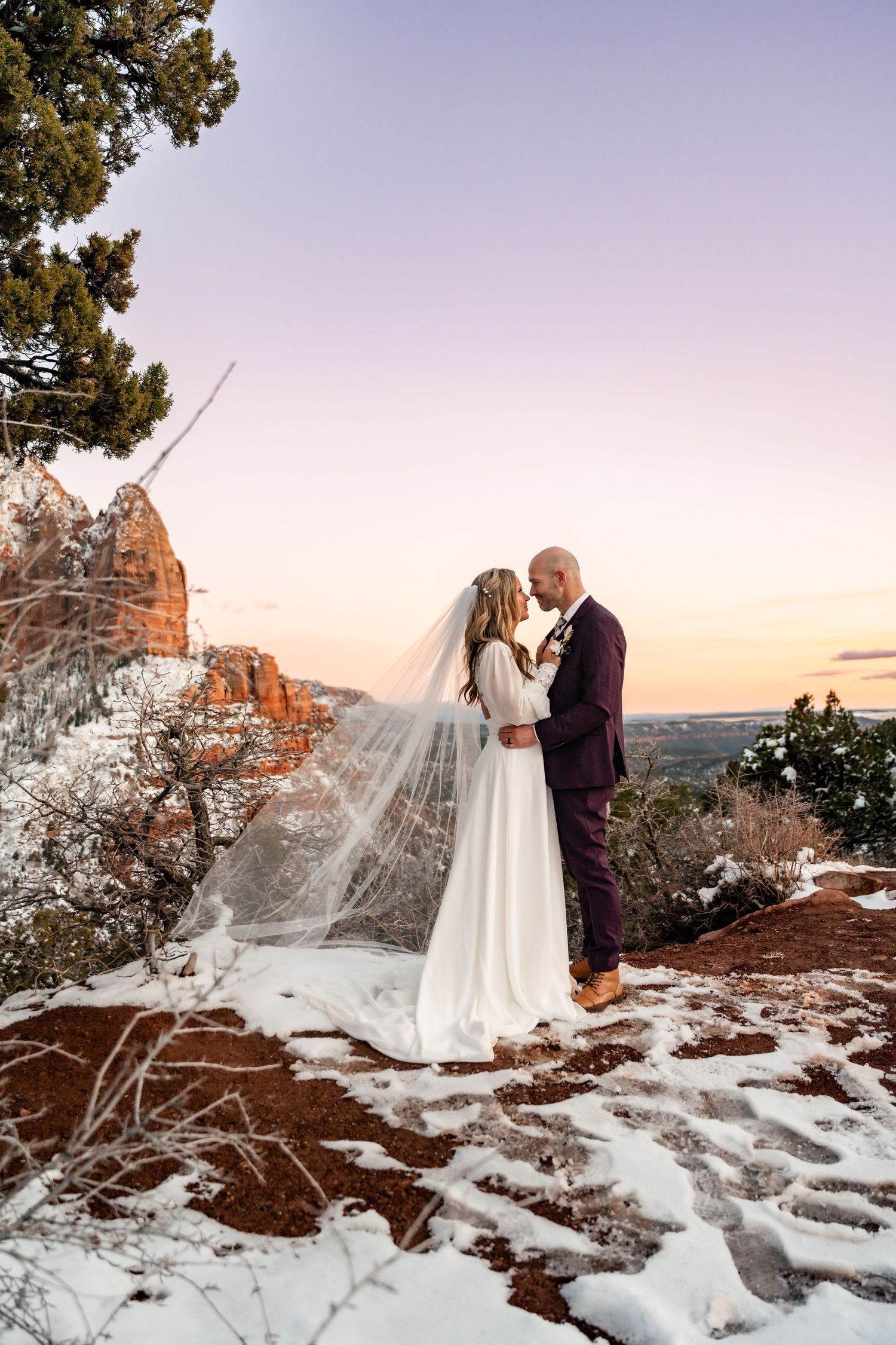 Winter wedding ceremony among snow-covered red rocks at sunset with dramatic mountain backdrop.