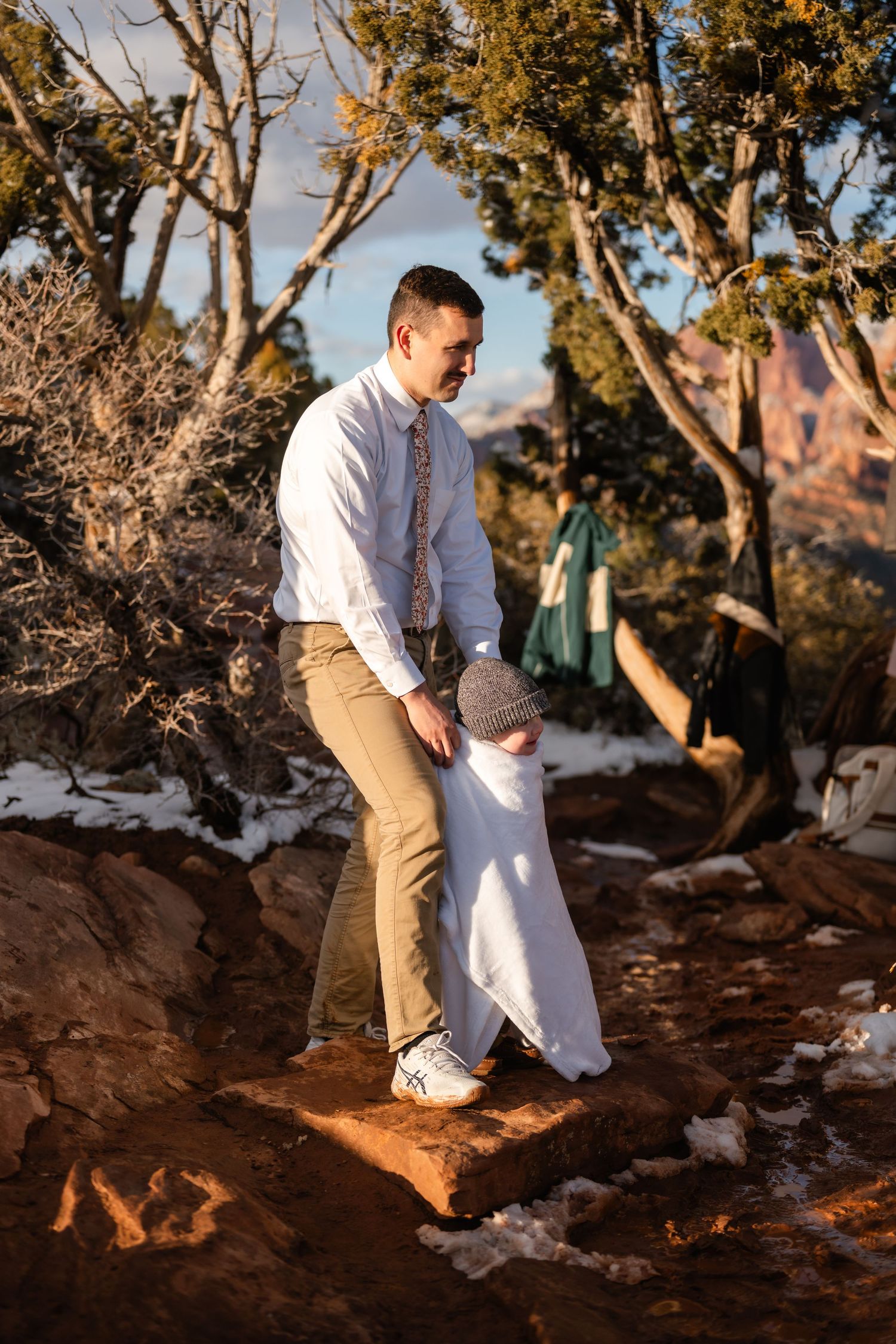 Couple standing together on snowy red rock formations during sunset.