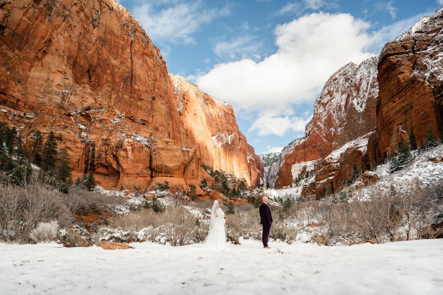 Snow-covered canyon trail winding between towering red rock walls.
