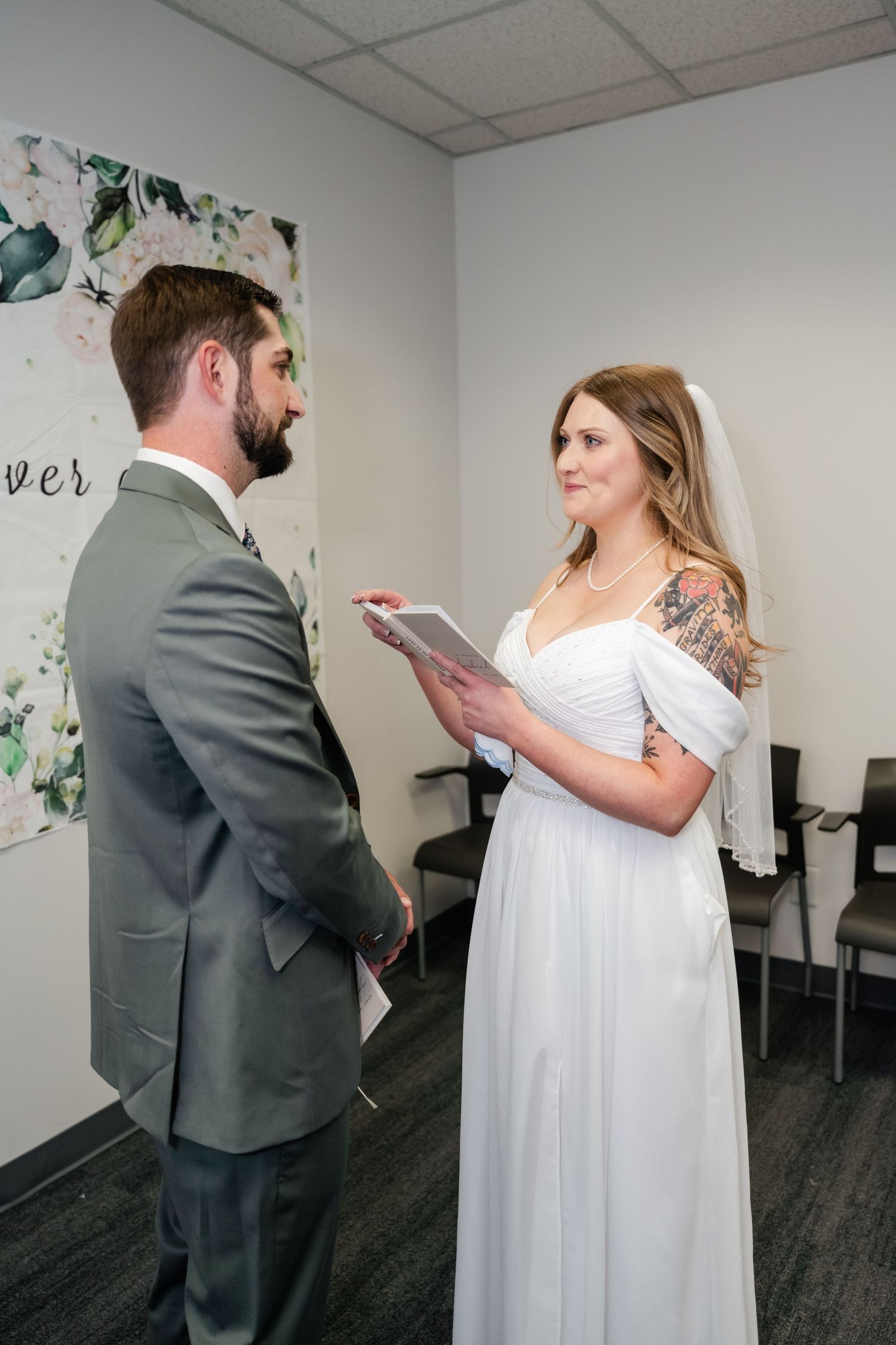 A wedding ceremony taking place in a simple room with floral wall decor.