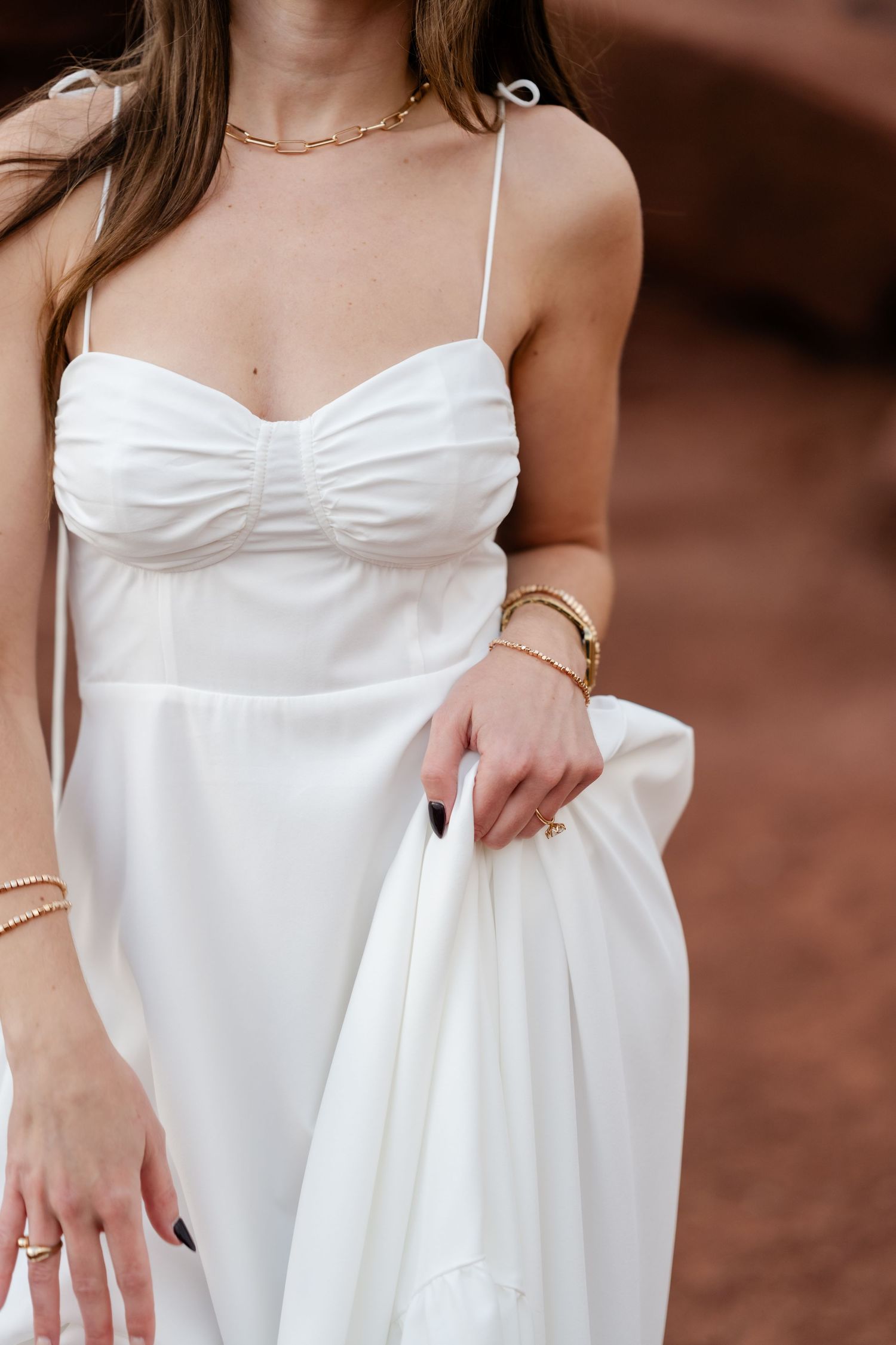 White strapless dress with delicate gold jewelry accessories photographed against red rock background.