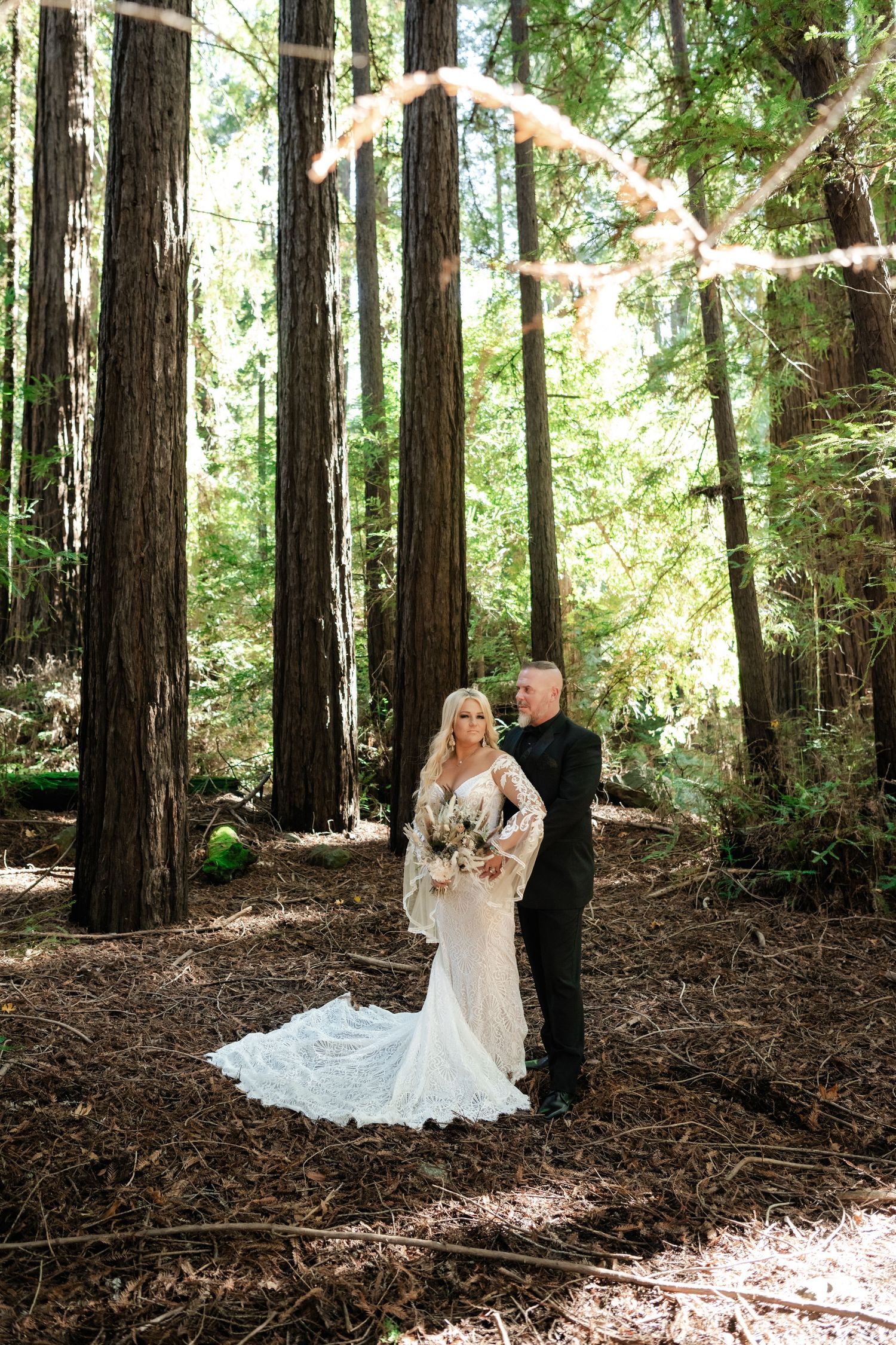 A romantic wedding photo session in a serene redwood forest with sunlight filtering through tall trees.