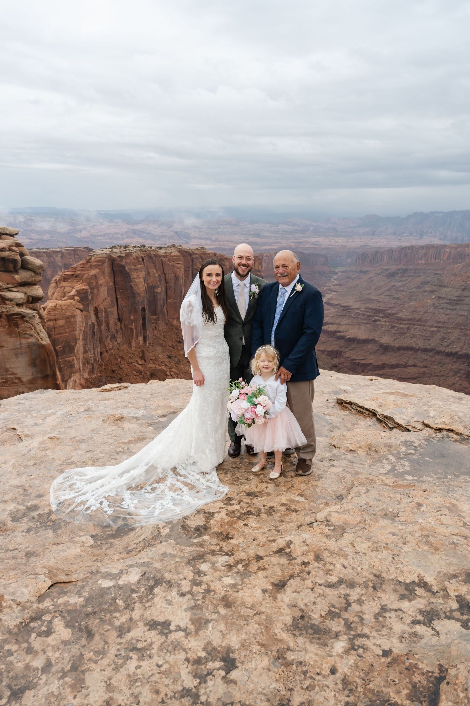 Wedding ceremony participants gather on rocky canyon overlook with dramatic desert vista.