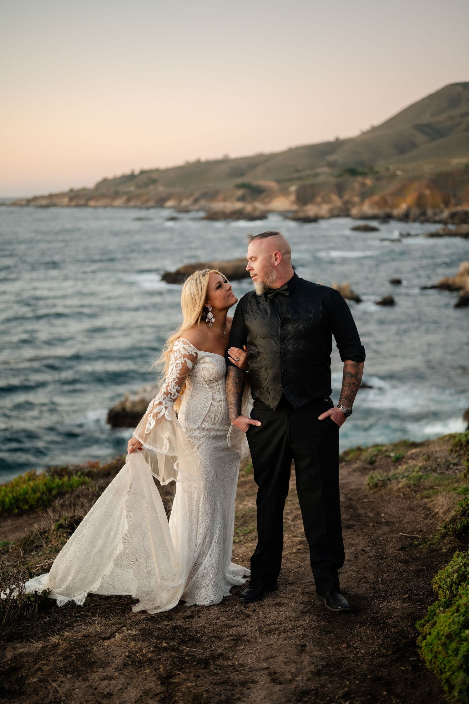 Wedding couple embraces on a scenic coastal bluff with waves crashing against rocks in the background.
