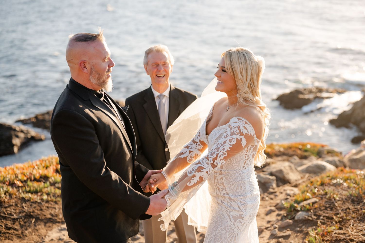 A wedding ceremony takes place on a scenic coastal cliff during golden hour as the sun sets over the ocean.