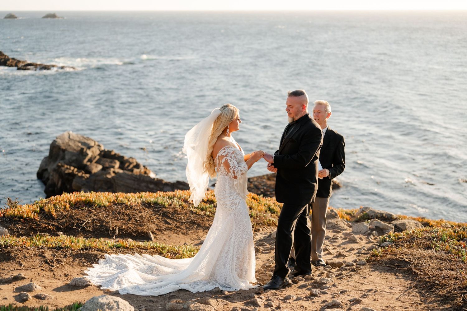 A wedding ceremony takes place on a scenic coastal cliff overlooking the ocean at sunset.