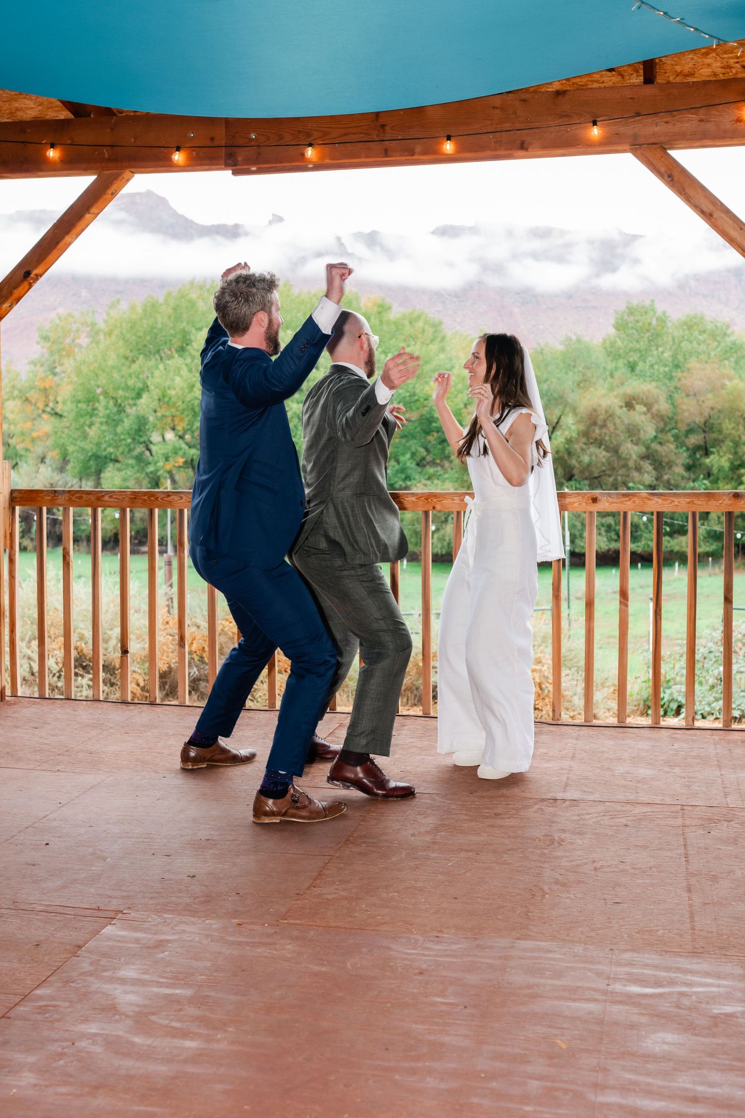 Wedding guests dancing and having fun on a covered outdoor patio with string lights and scenic views.