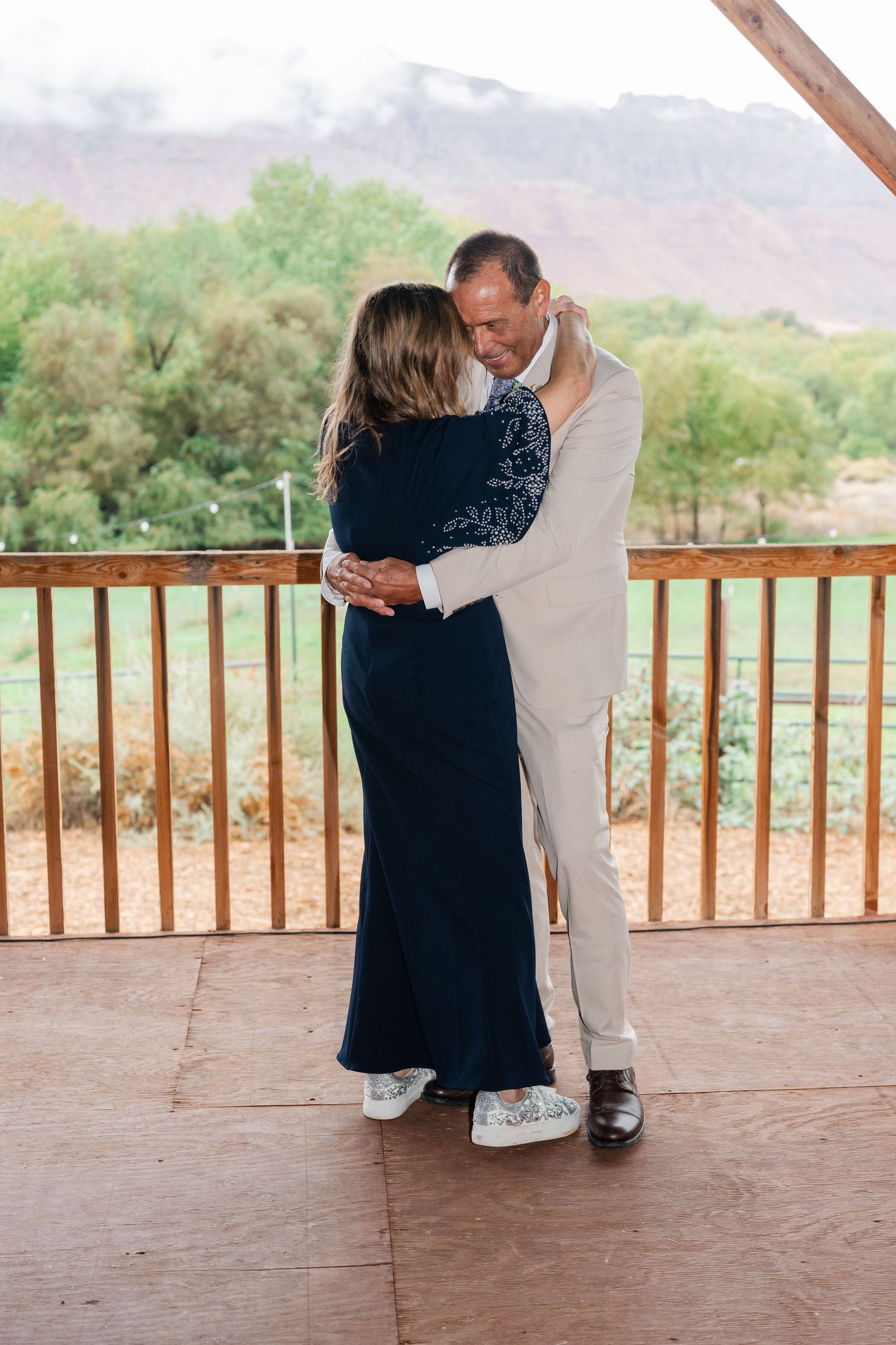 Couples slow dance on a covered patio during sunset with mountain scenery in the background.