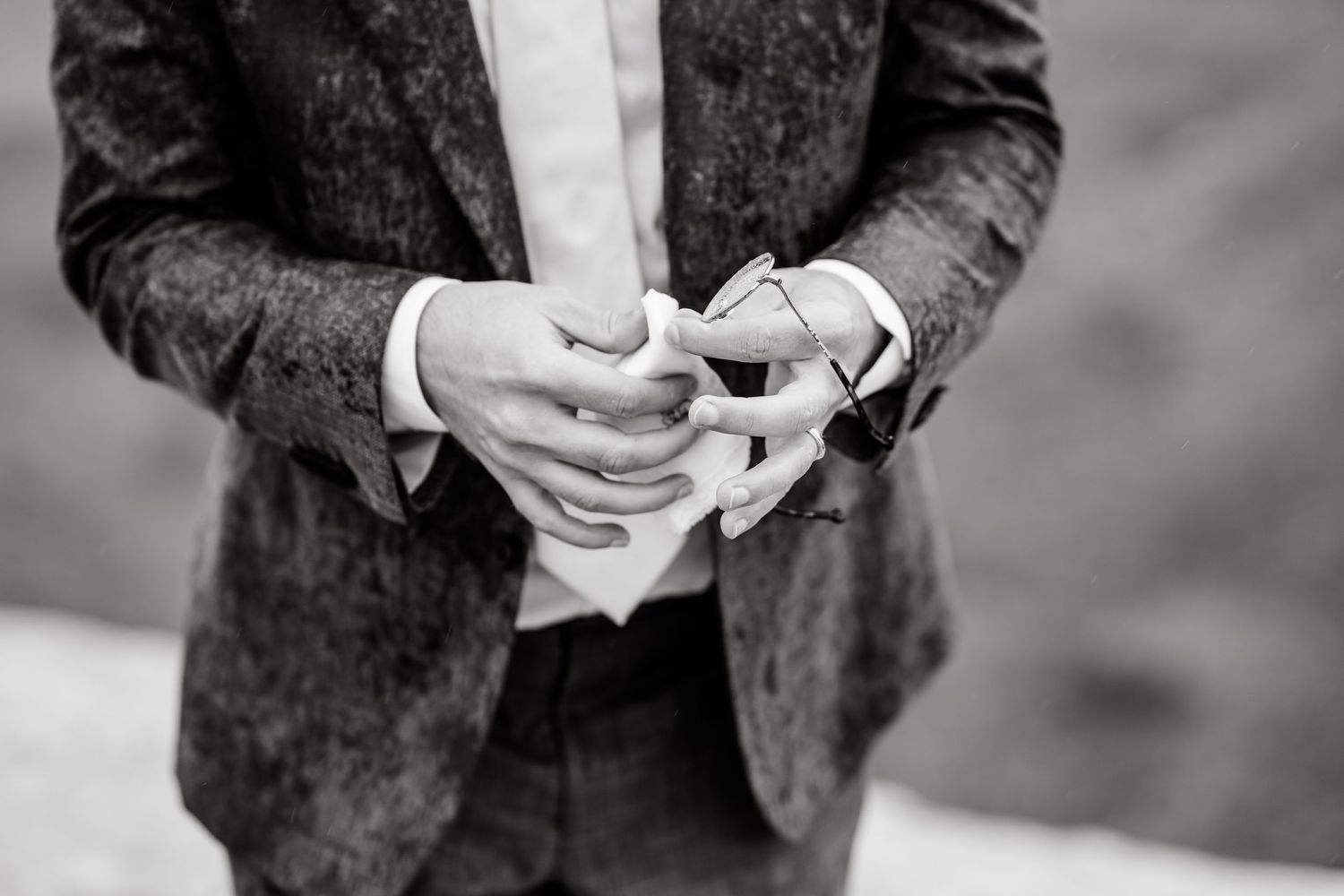 A person in a dark suit and white shirt holding a small white cup of coffee or espresso.