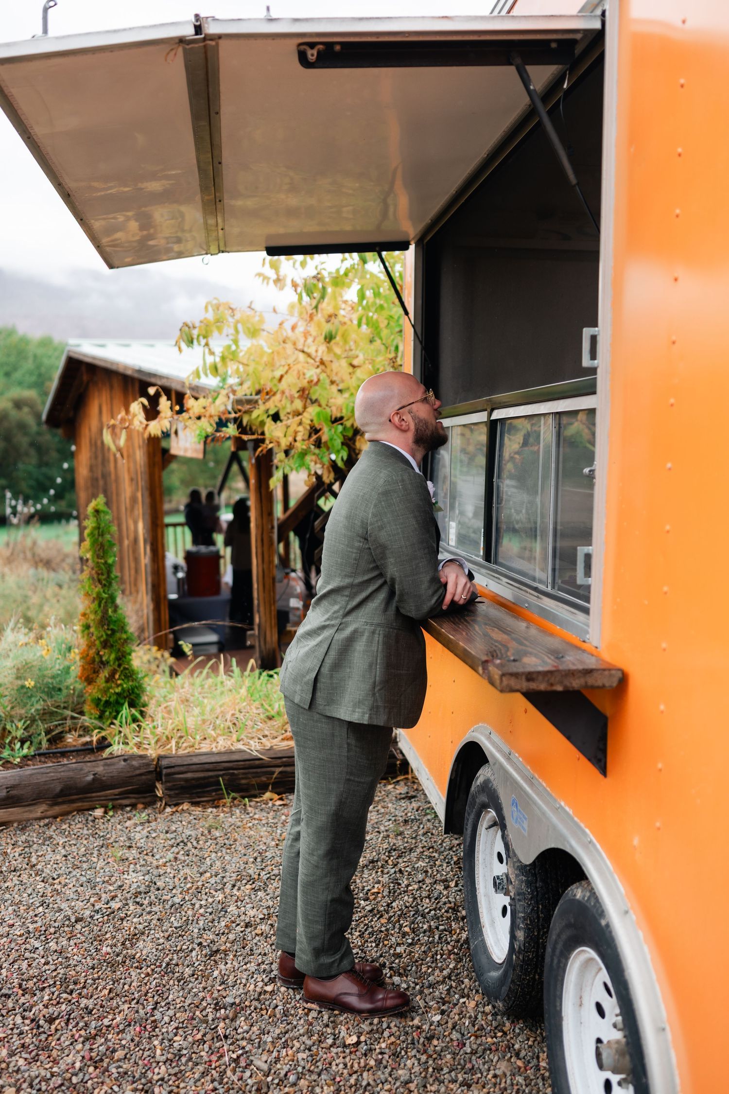 People ordering food from an orange food truck window at an outdoor venue.