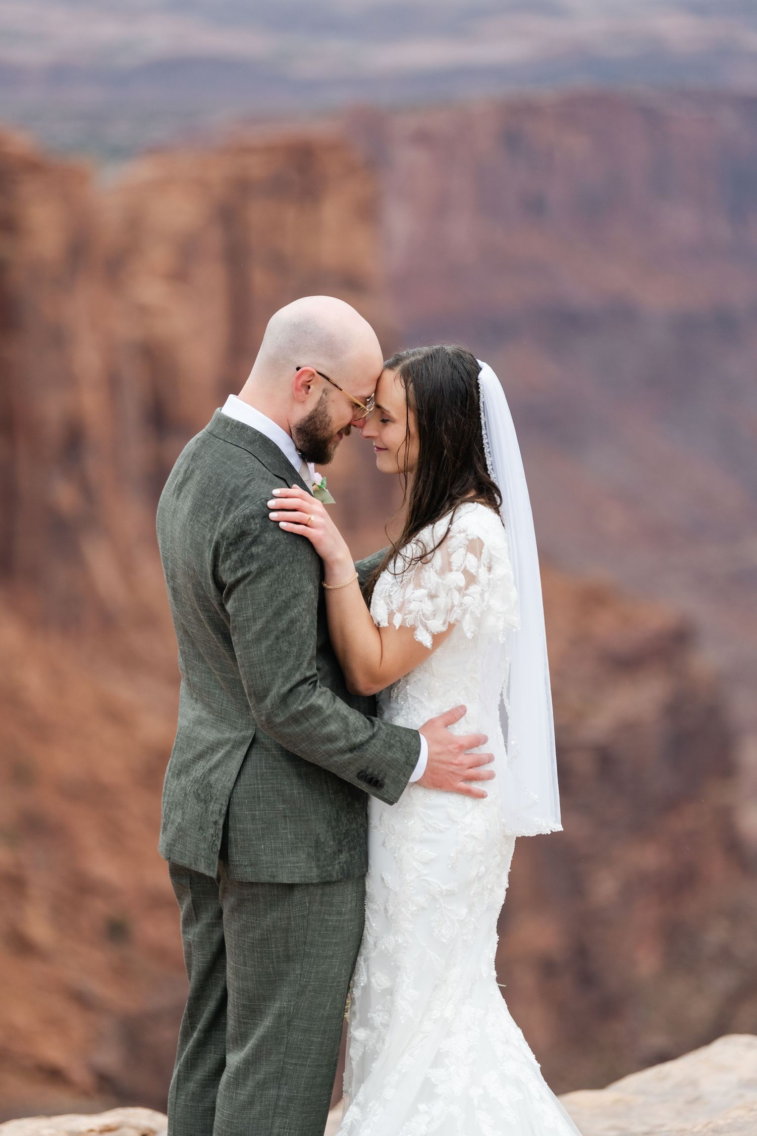 A bride and groom share an intimate moment against dramatic red rock canyon cliffs.
