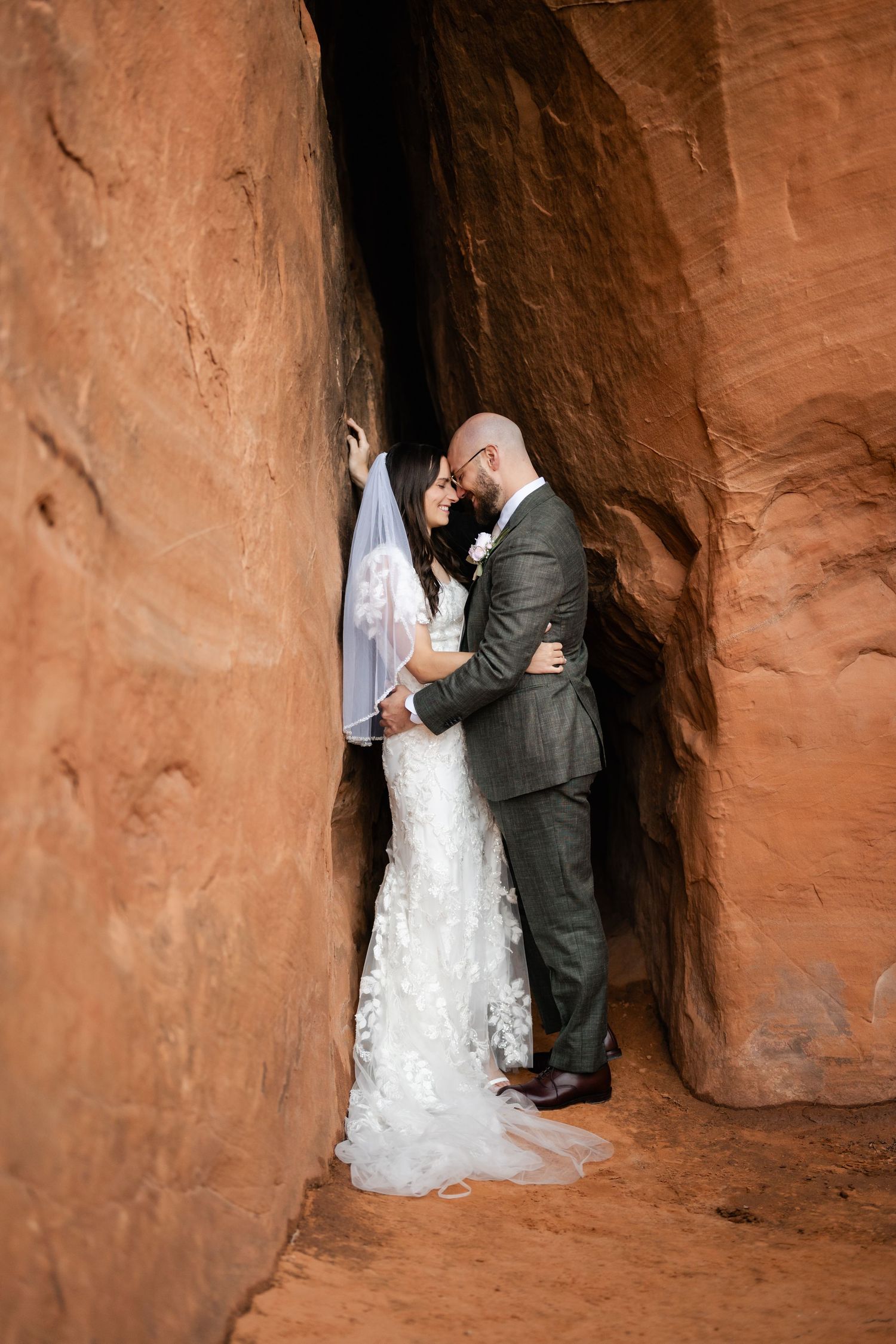 A romantic wedding moment captured in a natural sandstone alcove with dramatic red rock walls.